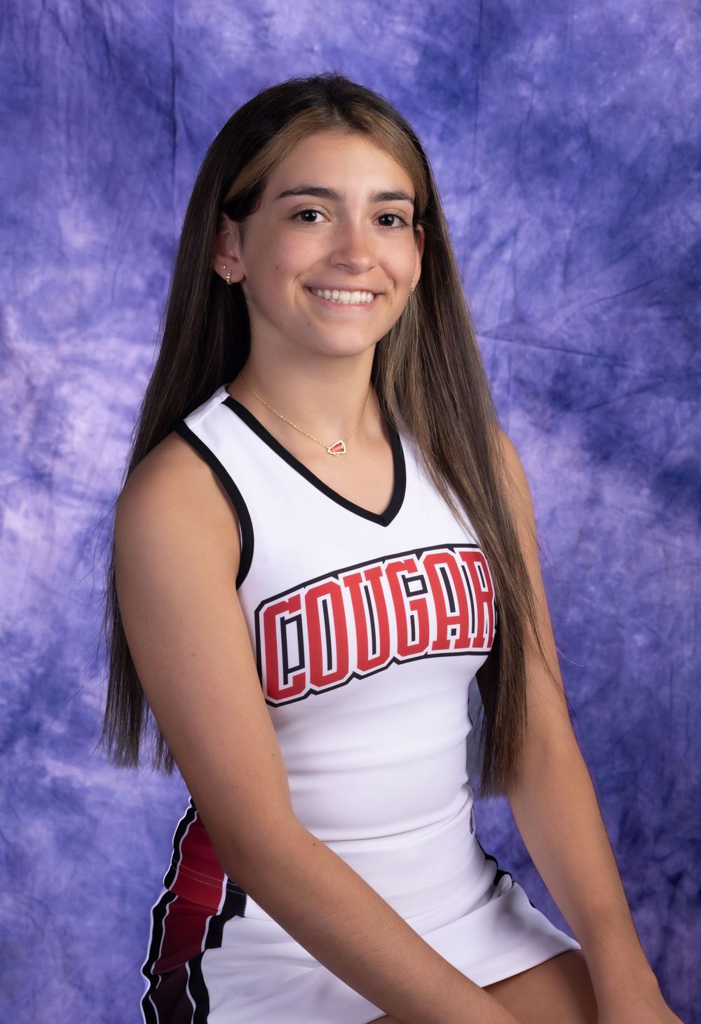 Smiling cheerleader in white Cougars uniform poses for portrait photo against blue backdrop.