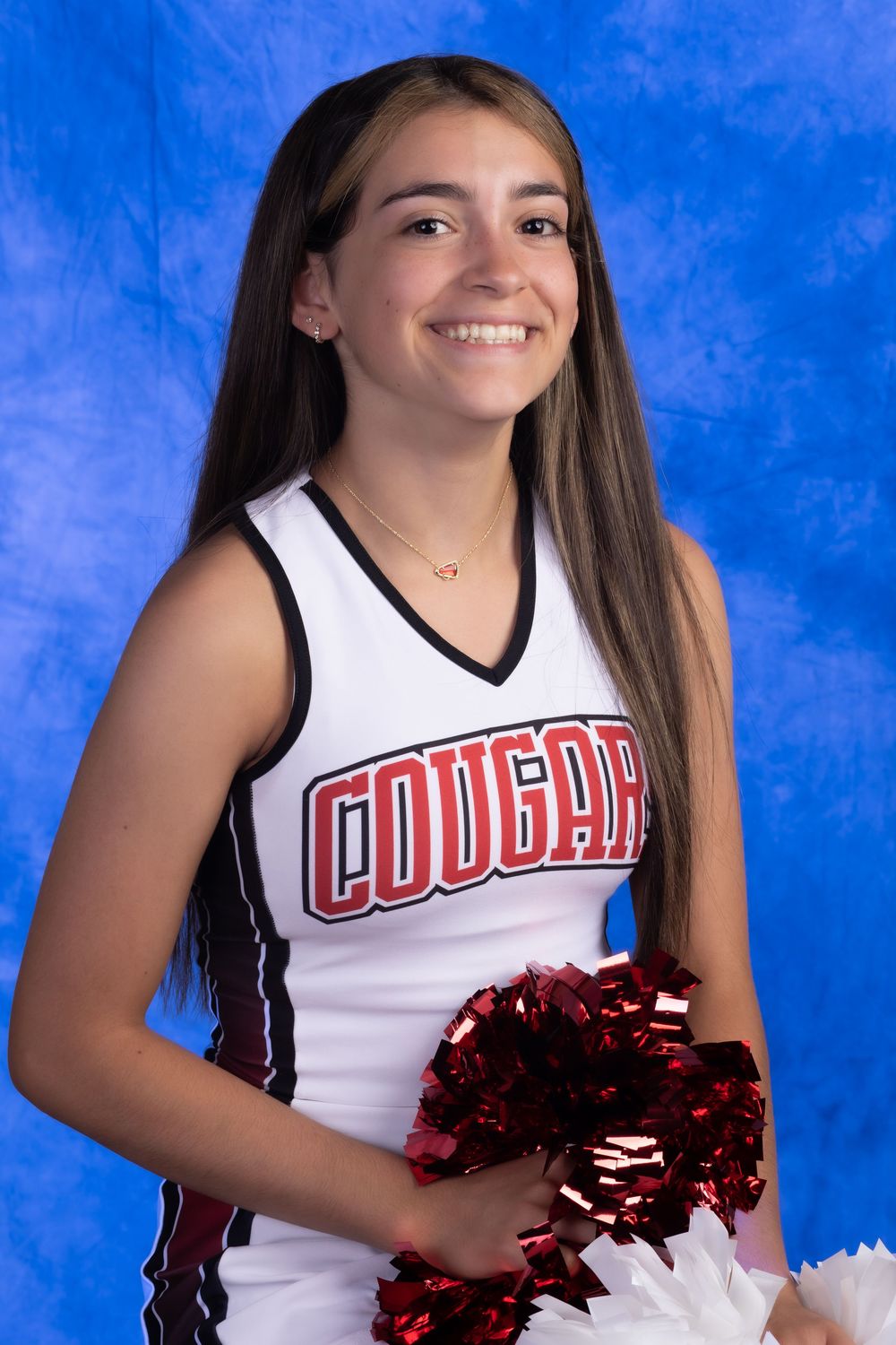 Smiling young cheerleader in white Cougars uniform holding red pom-poms against a blue background.