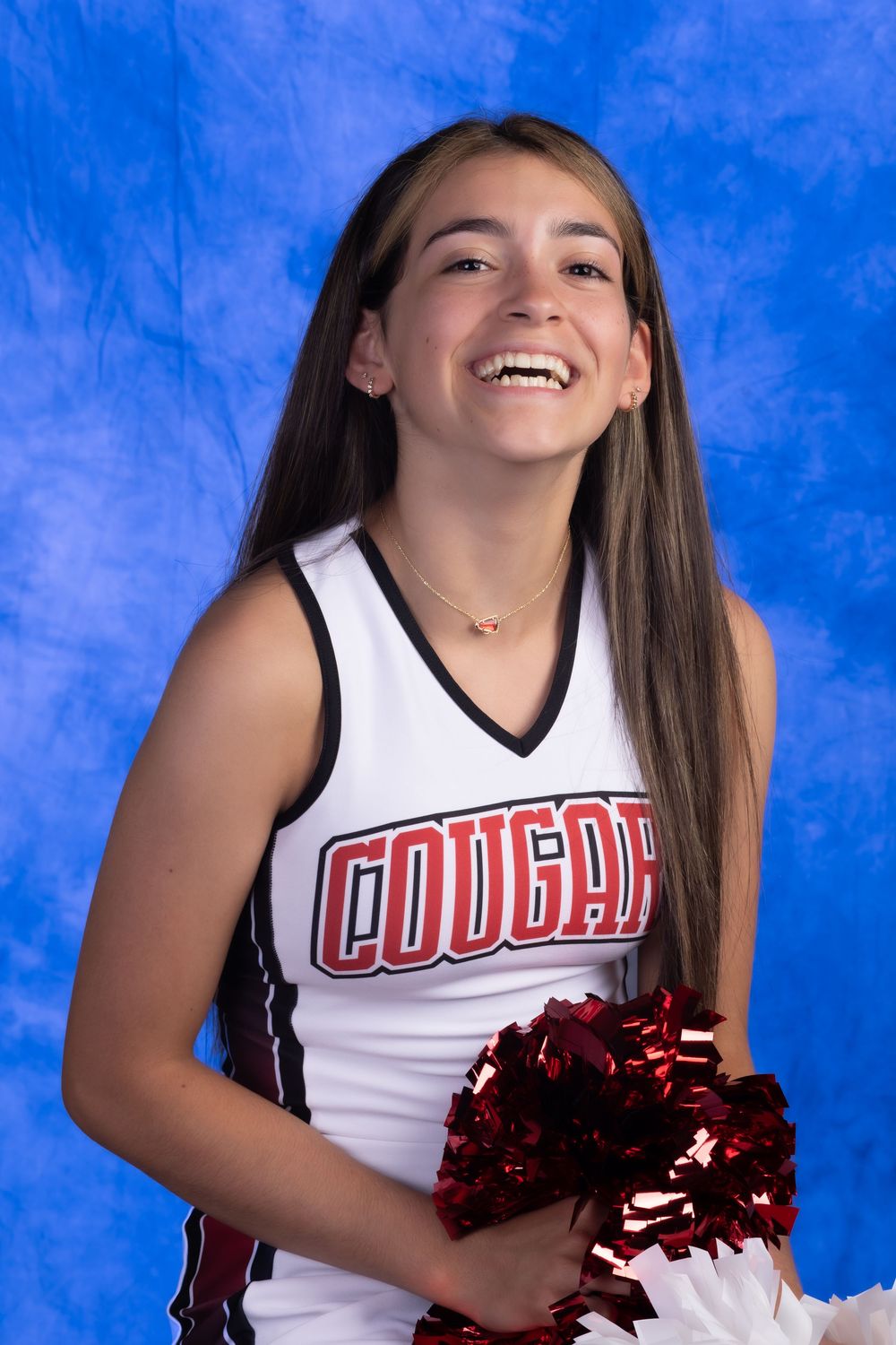 Smiling cheerleader in Cougars uniform holding red pom-poms against a blue background.