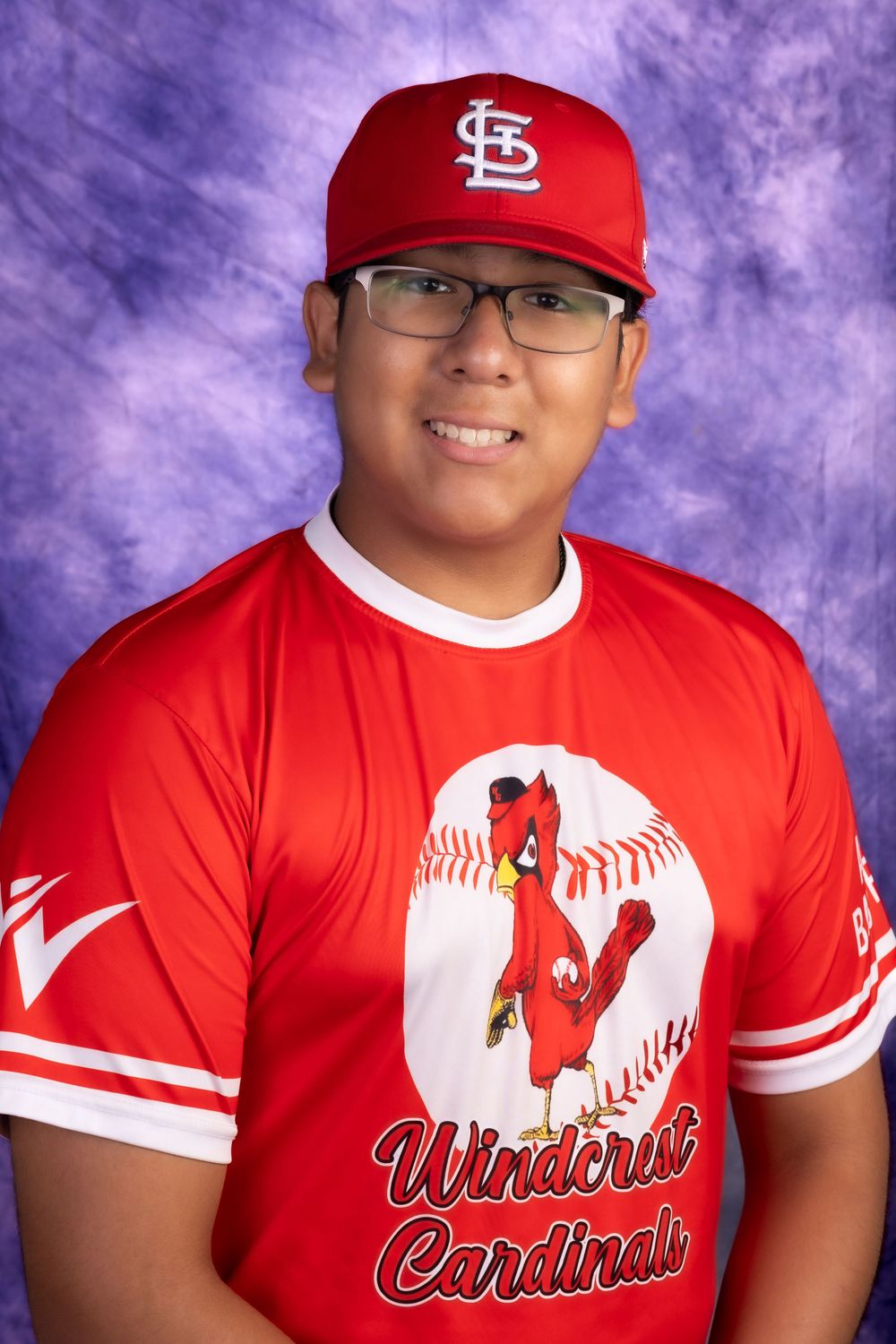 Smiling young baseball player wearing red Windcrest Cardinals jersey and matching cap.