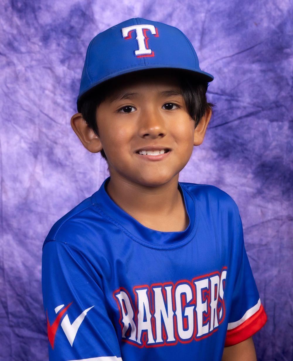Young boy in Texas Rangers blue baseball uniform and cap smiling for team photo.