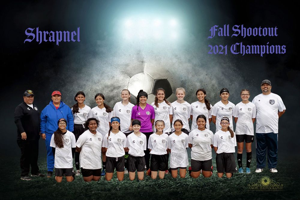Youth soccer team poses together in white uniforms on a field at night under stadium lights.