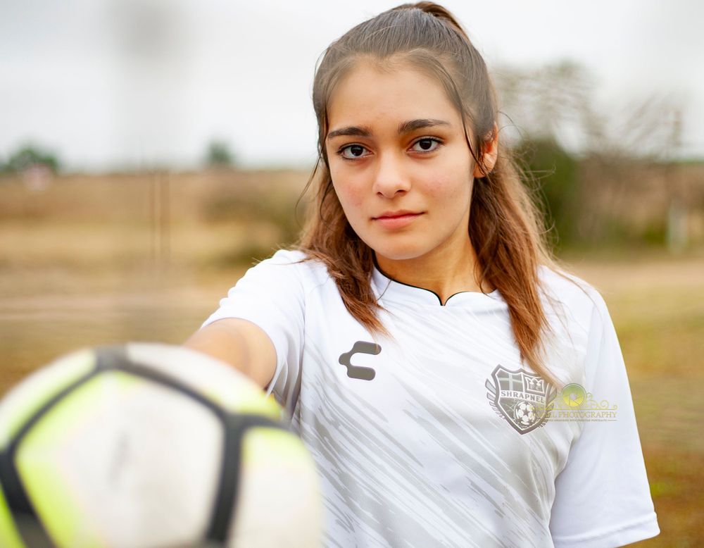 Soccer player in white jersey poses with ball on field during outdoor practice session.