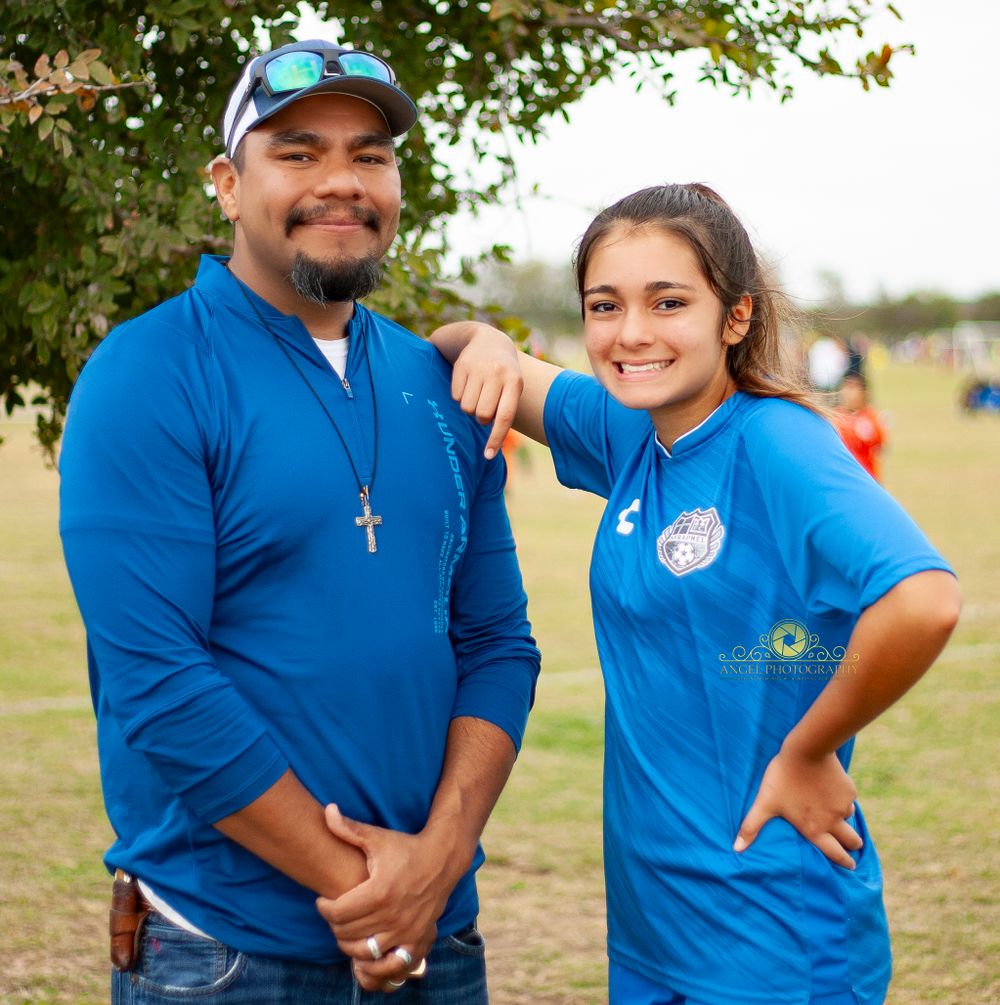 Coach and player in matching blue uniforms pose together outdoors.