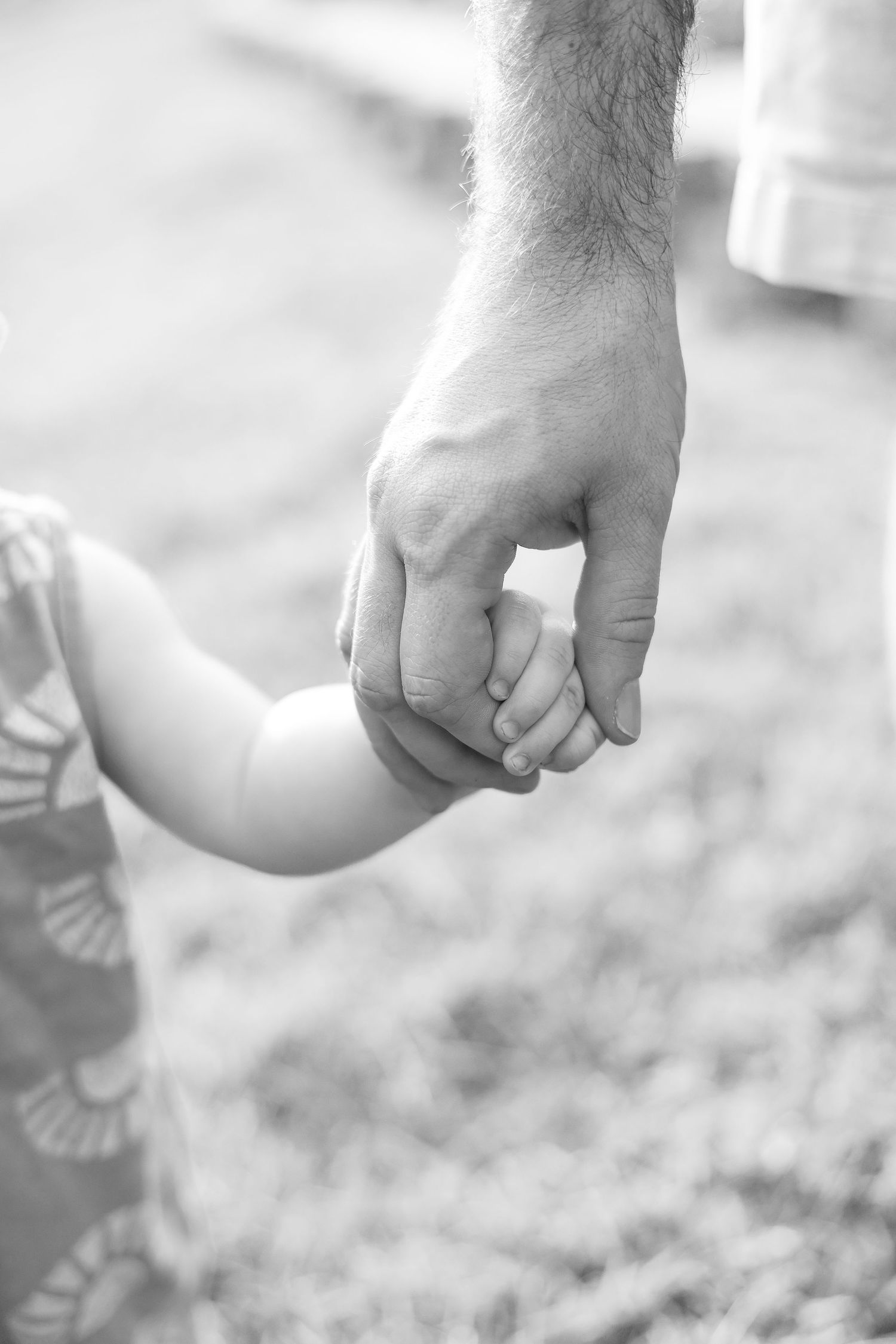 Black and white image of parent and child holding hands outdoors.