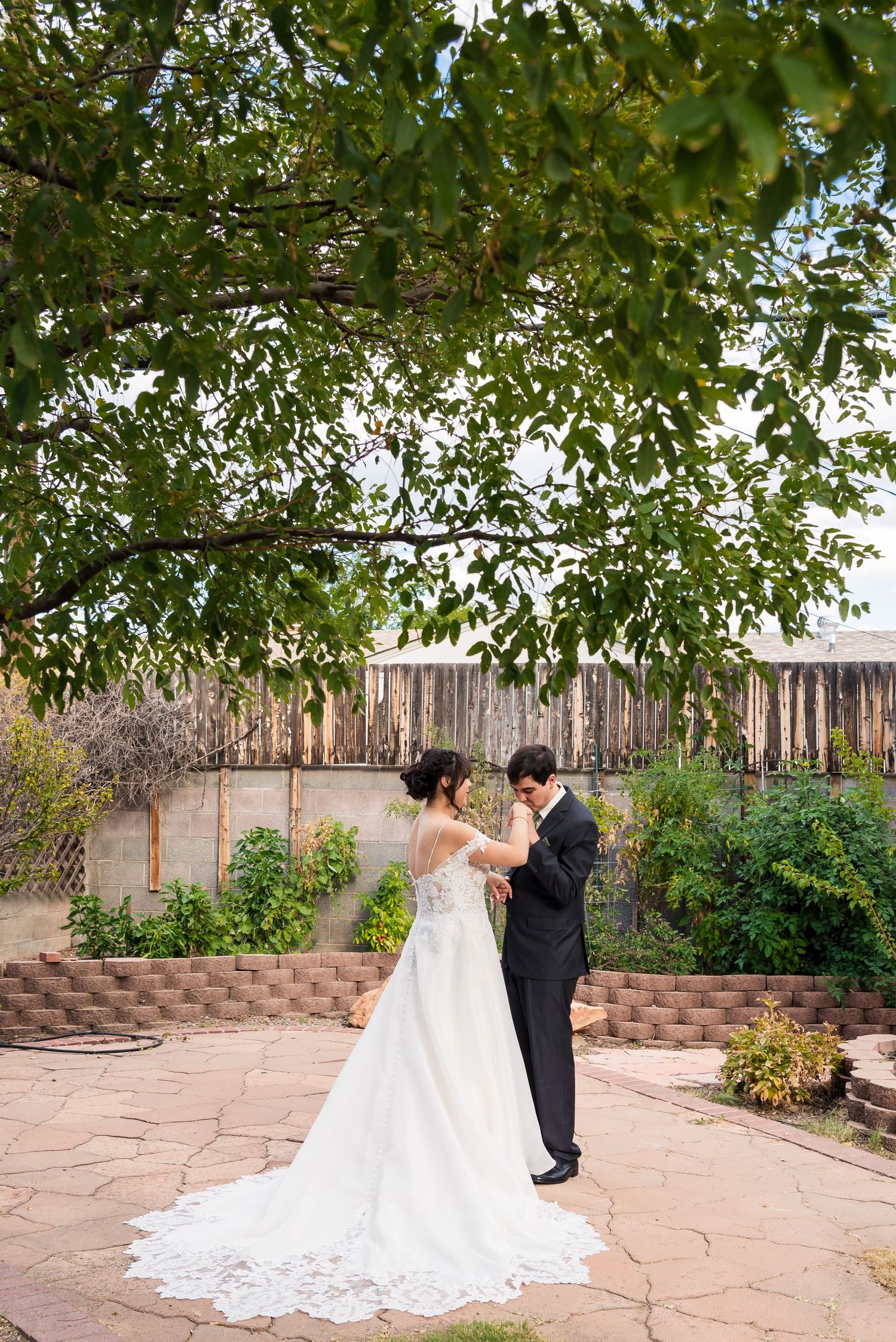 Couple dancing on stone patio under green tree canopy at wedding venue.