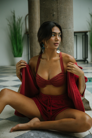 Woman in red lingerie posing artistically on floor near decorative stone columns.