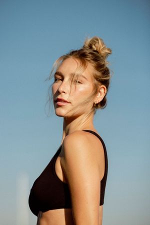 Portrait against blue sky showing black athletic top and natural makeup in warm sunset lighting.