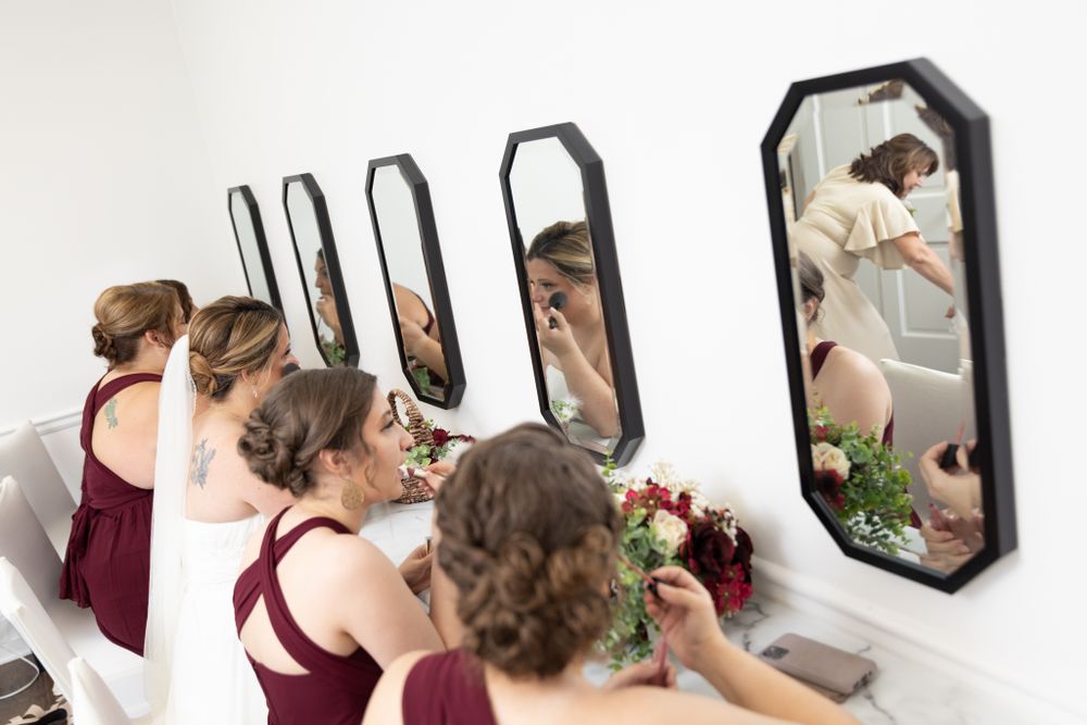 Bridesmaids and bride finish makeup in row of mirrors lining wall