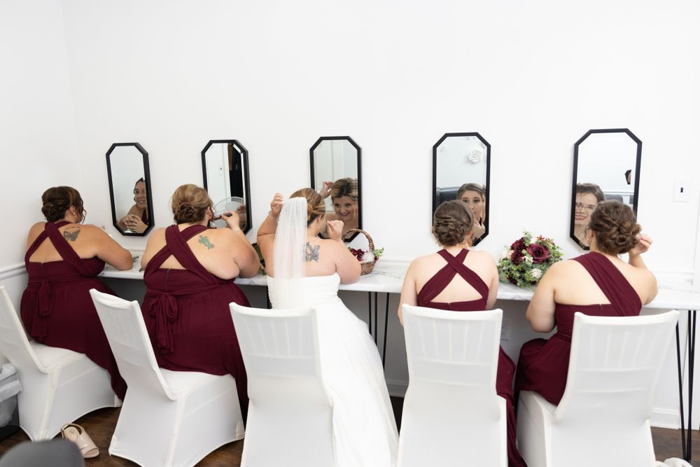 Bridesmaids and bride finish makeup in row of mirrors lining wall