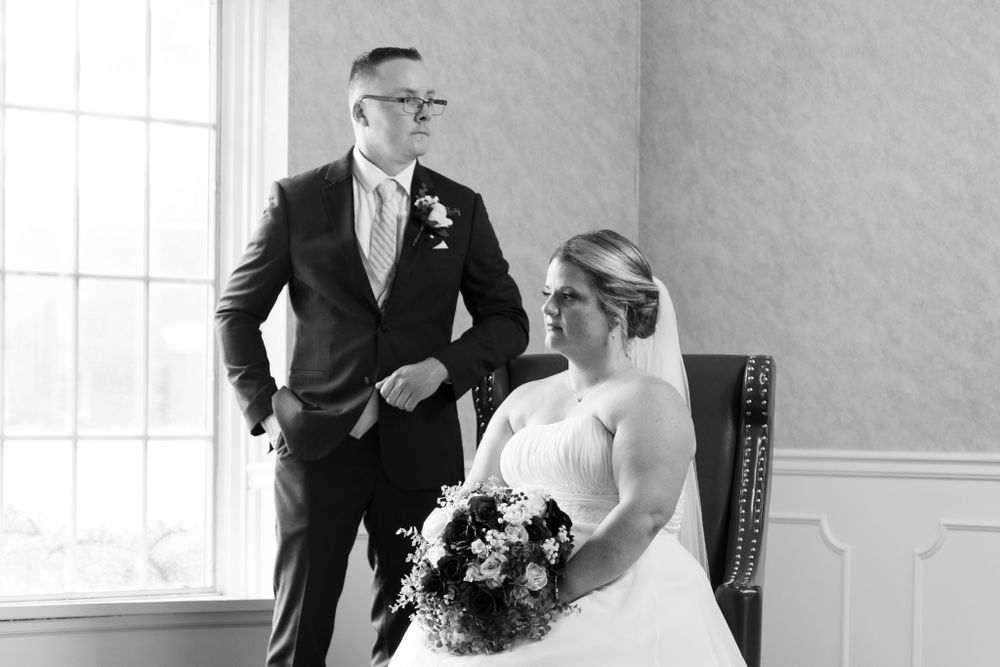 A black and white wedding portrait of newlyweds seated in an elegant room with natural lighting.