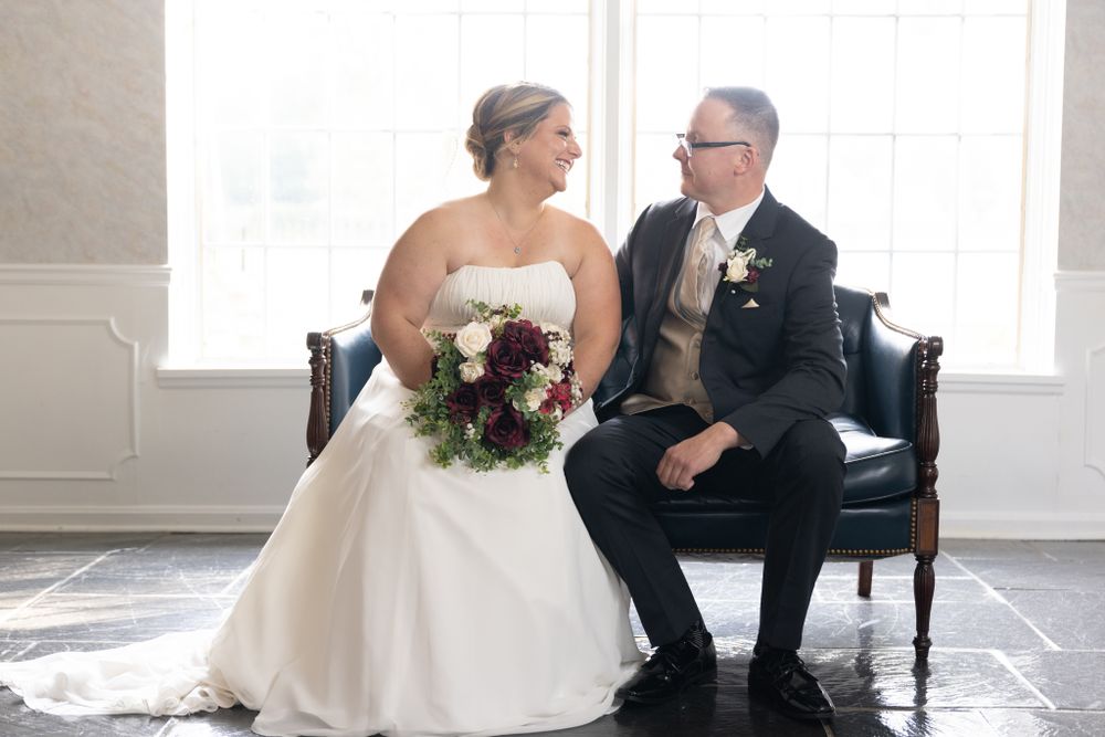 A couple shares an intimate moment sitting together on a vintage chair during their elegant wedding photoshoot.