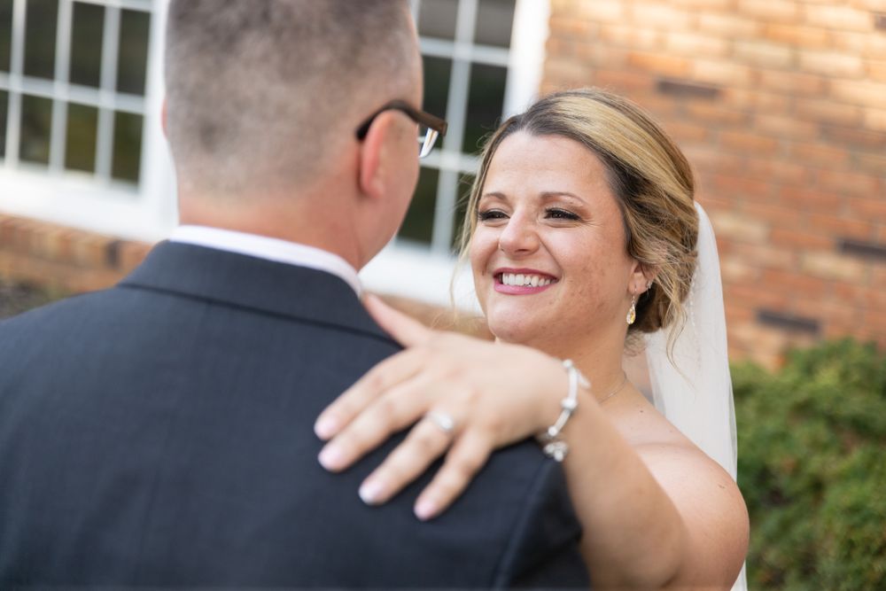 A candid moment between newlyweds with a brick building and greenery in the background.