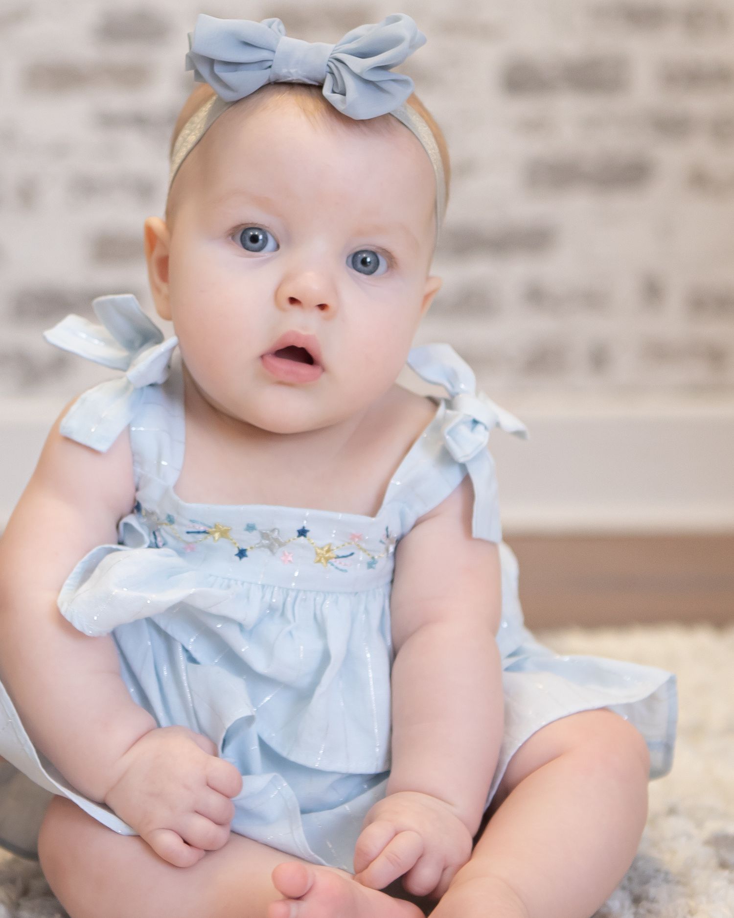 Baby wearing light blue dress and bow headband in portrait sequence.