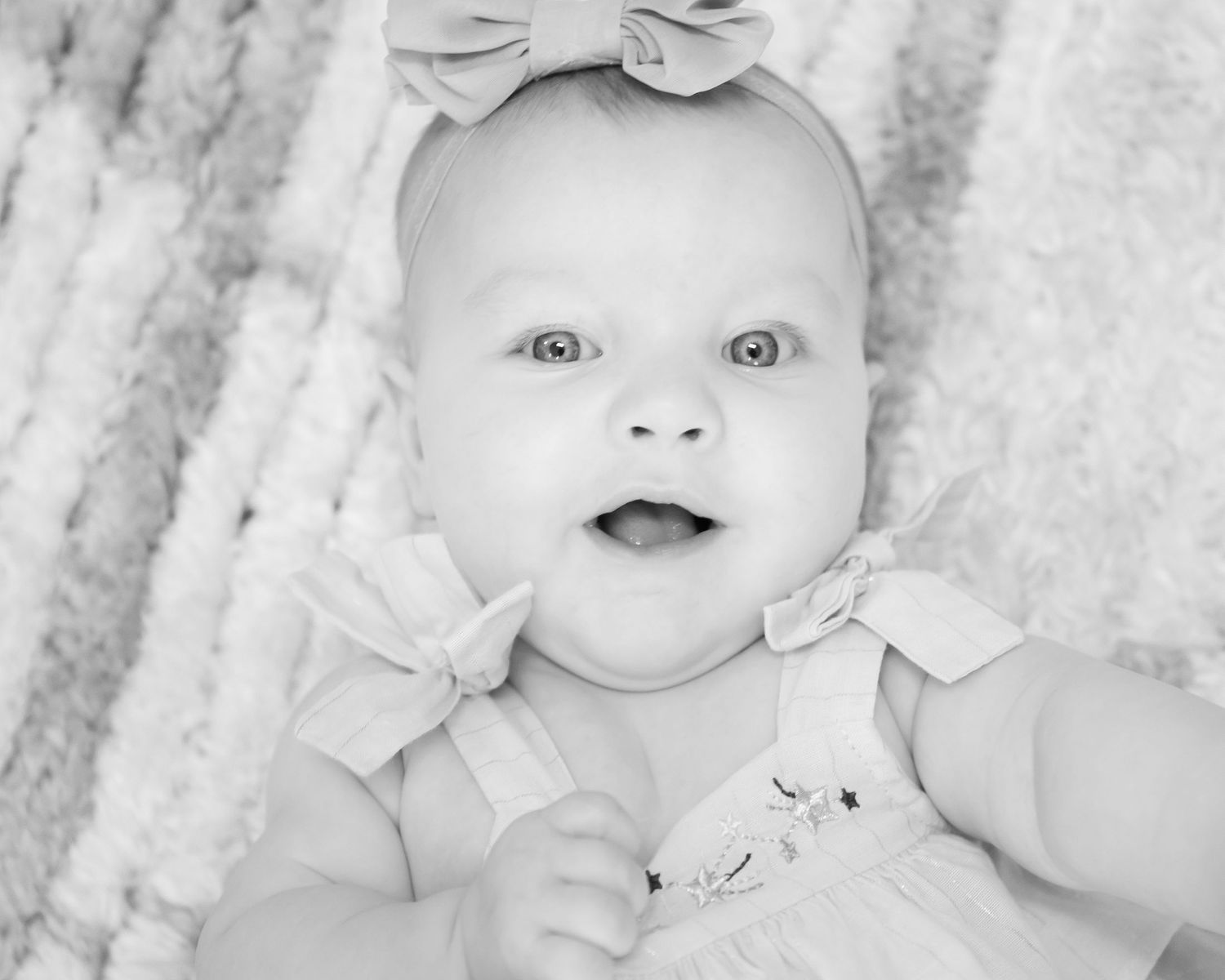 Black and white portraits of infant wearing bow headband against textured background.