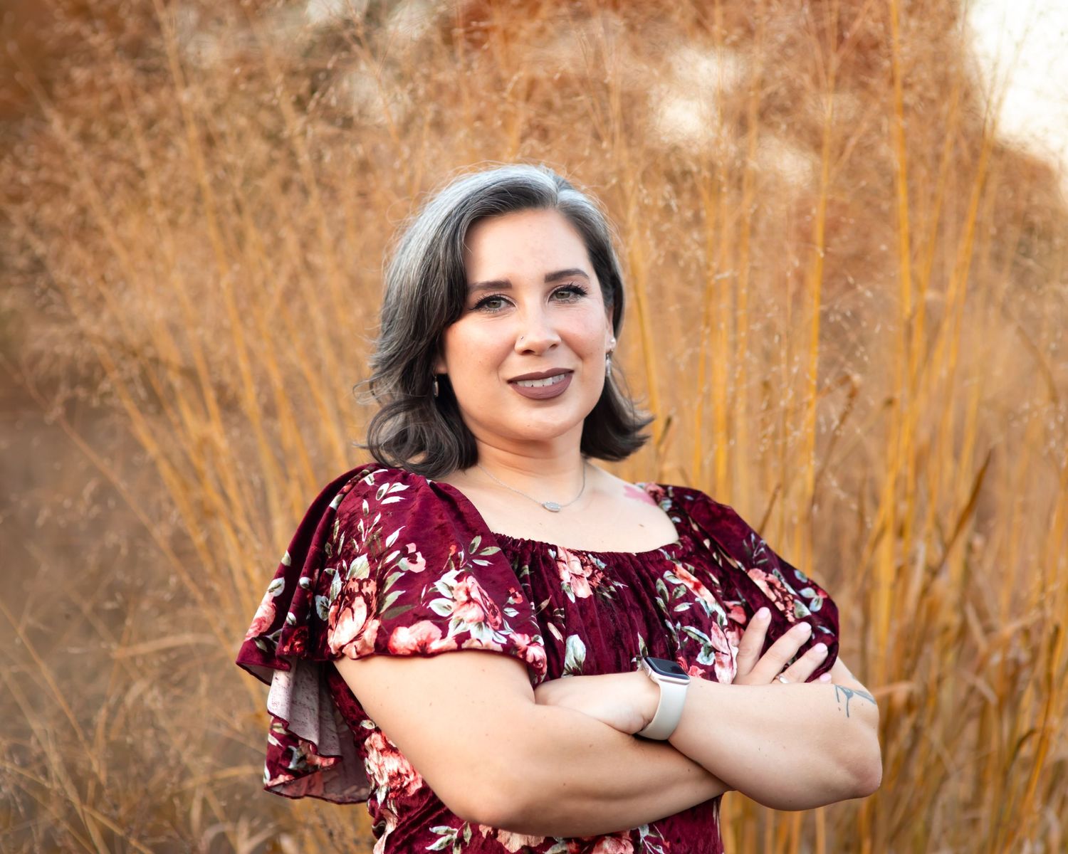 Person in burgundy dress poses against autumn foliage background.