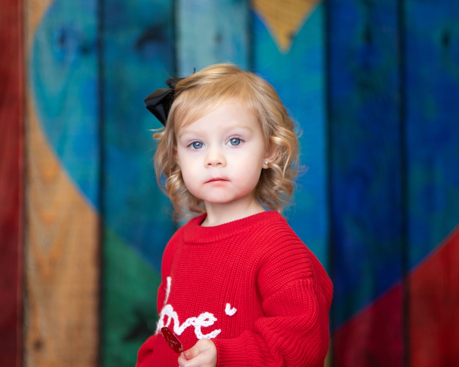 Young child in red sweater photographed against vibrant blue background.