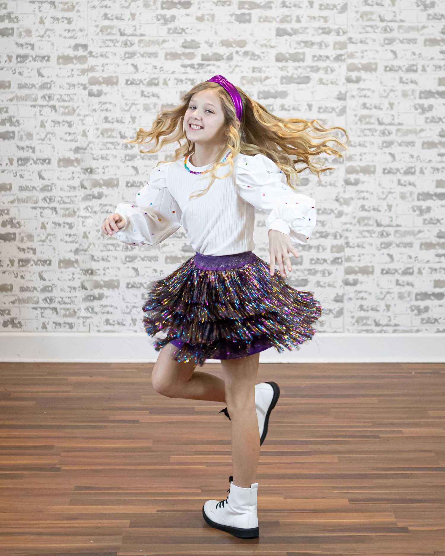 Child in a white top and sparkly tutu twirling and dancing on hardwood floor.