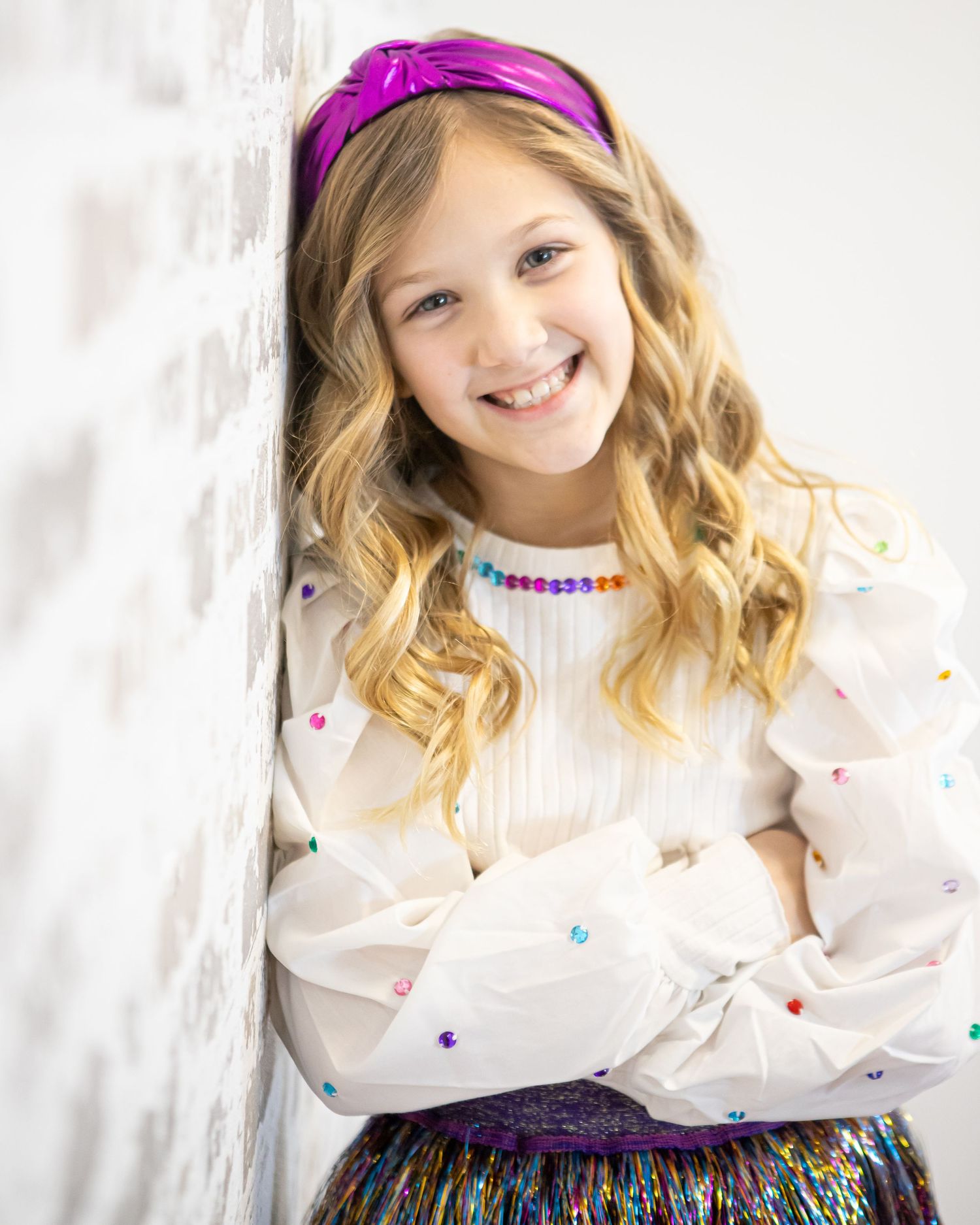 Portrait with purple headband and sparkly outfit against white background.