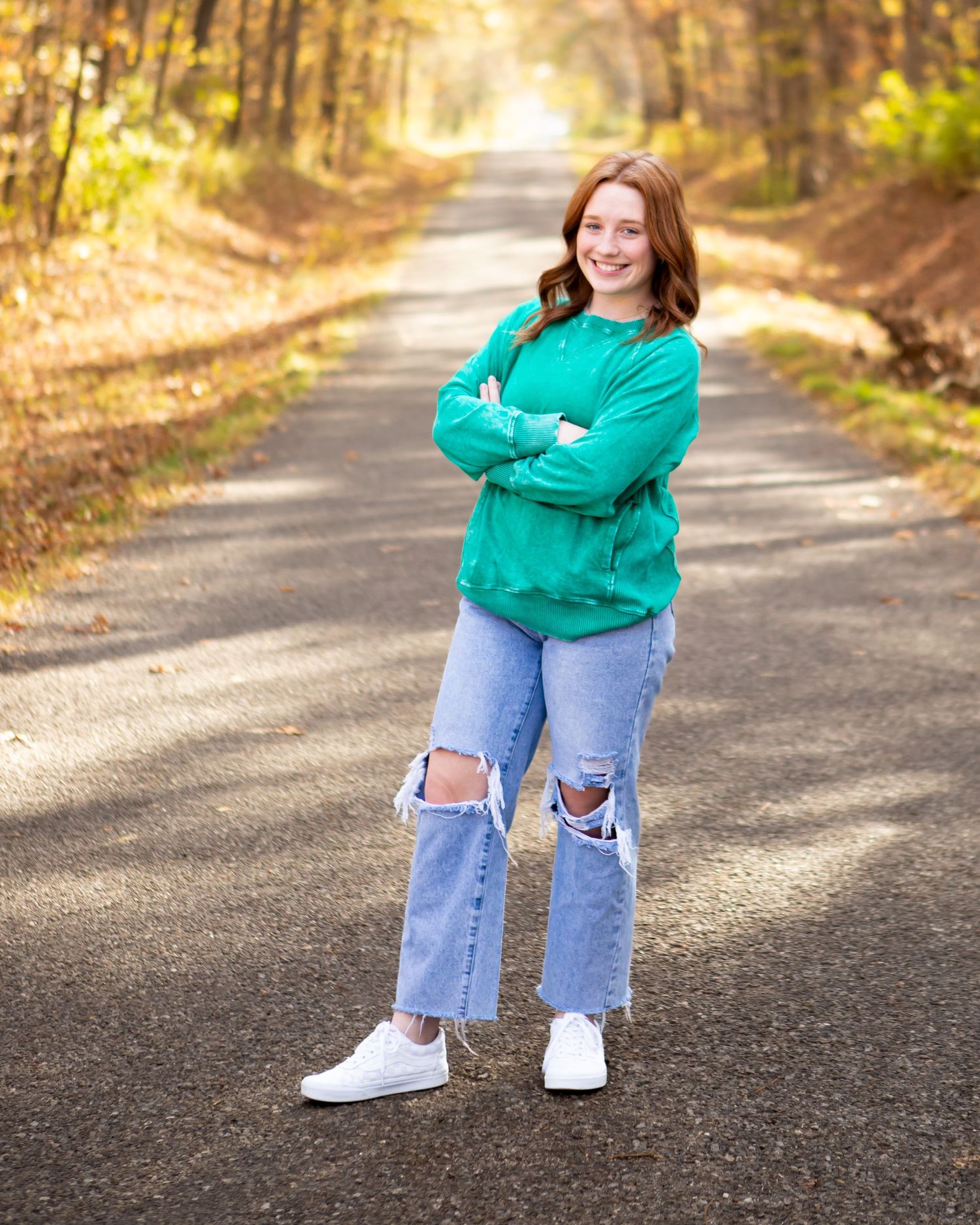 Casual portrait session on a fall path with ripped jeans and green sweater.