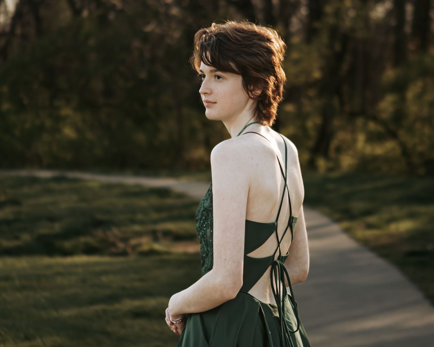 Outdoor portraits in a green dress walking along a sunlit path.