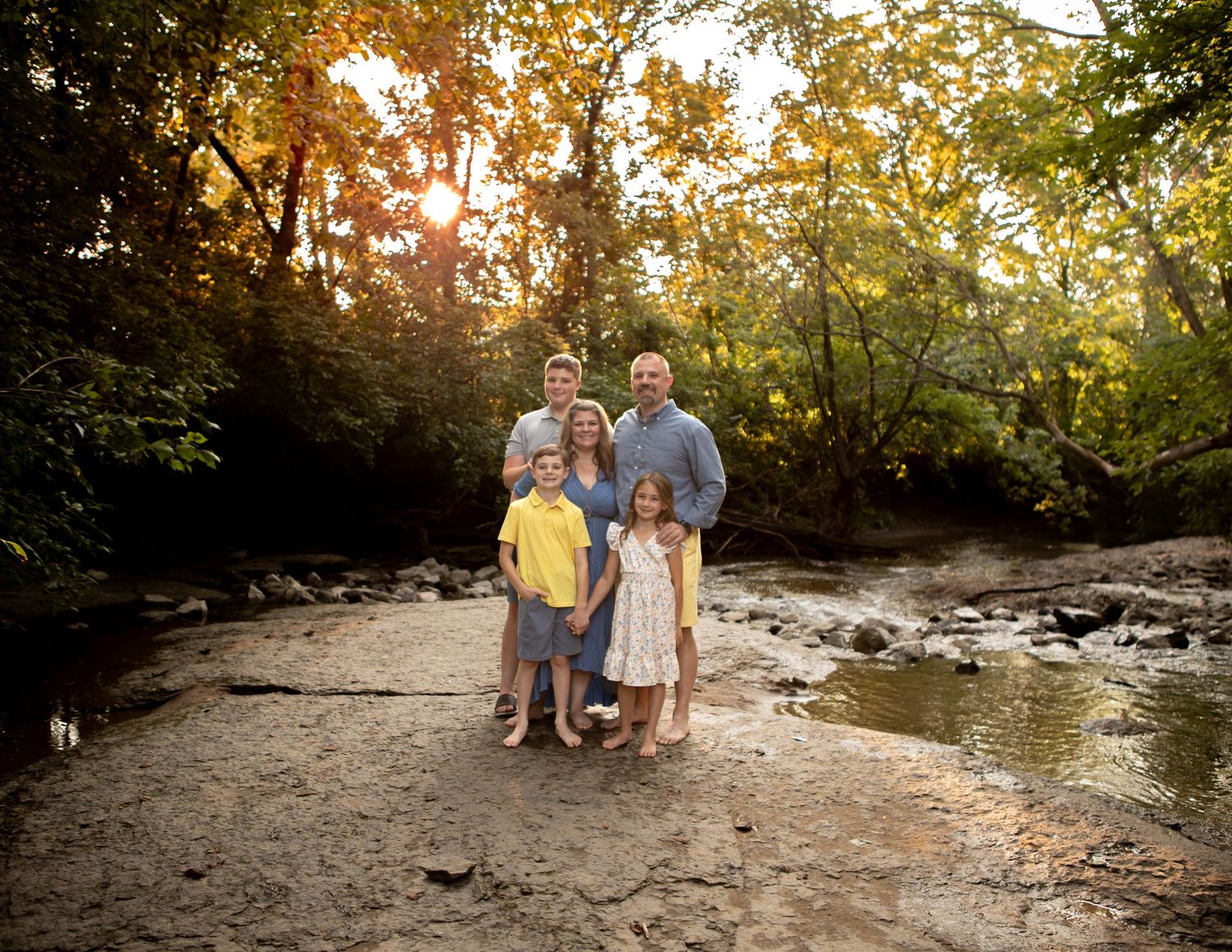 Group portrait session at a scenic creek with golden sunlight filtering through trees.