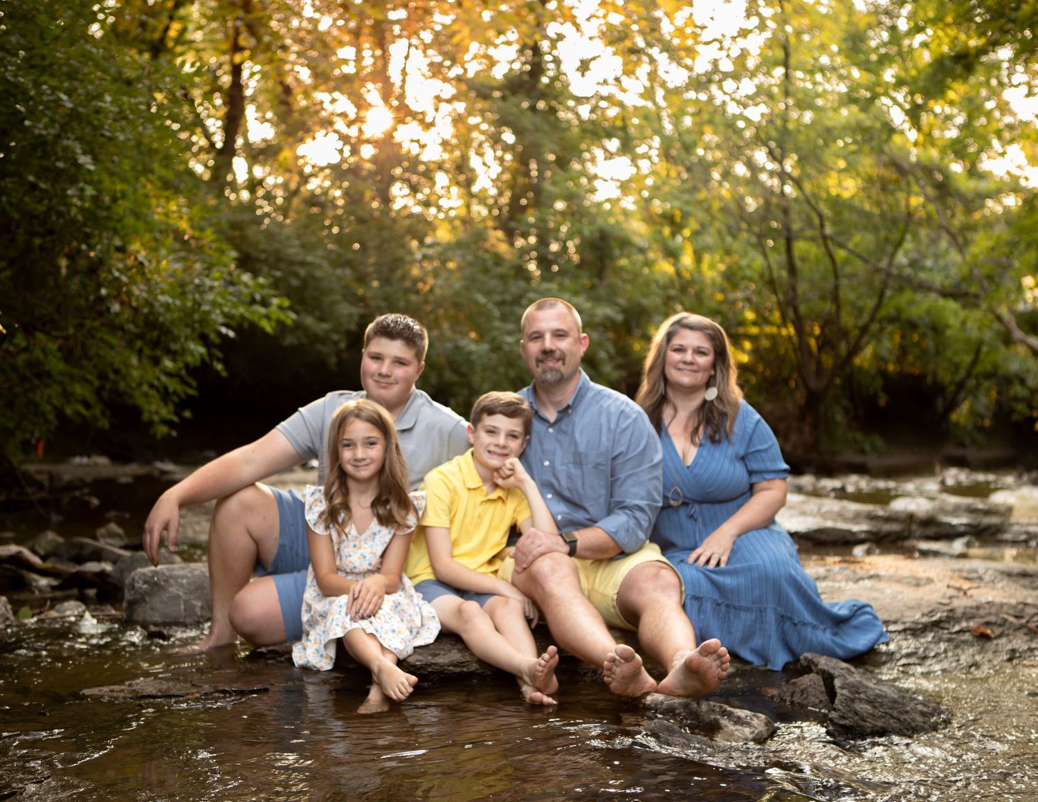 Family relaxing together on rocky creek bank during sunset photoshoot.