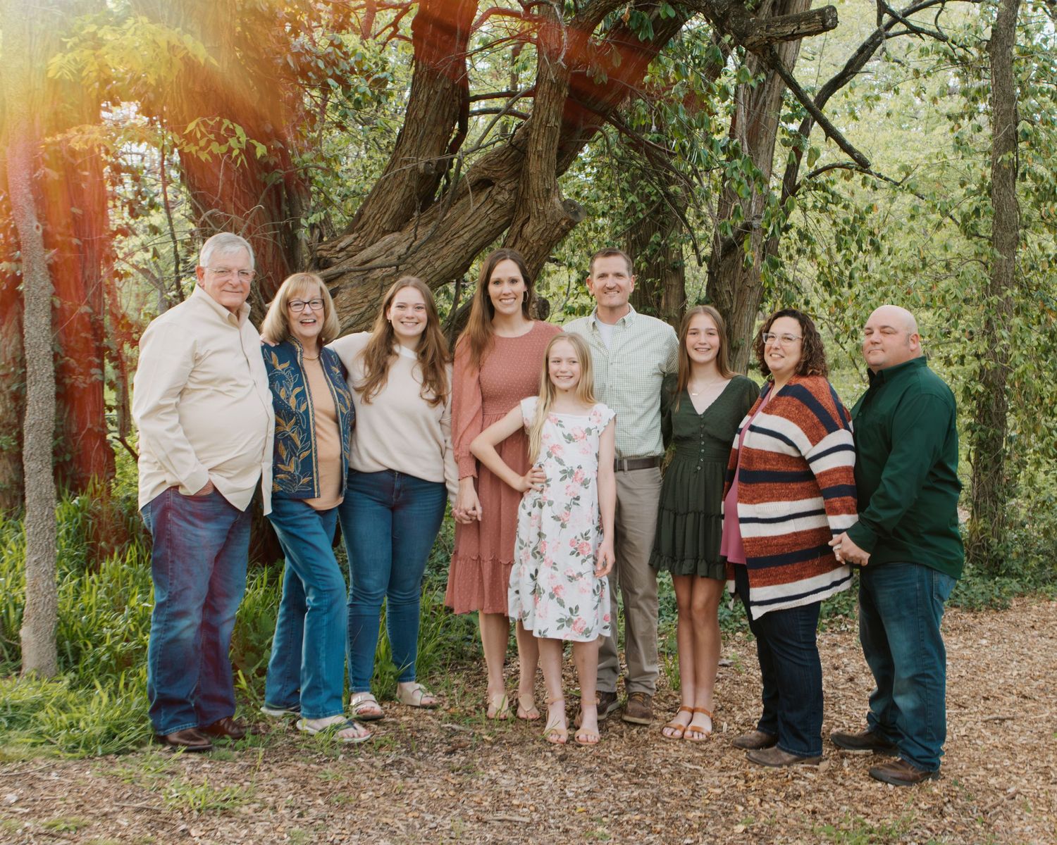 Extended family gathering for outdoor portrait session among trees in natural setting.
