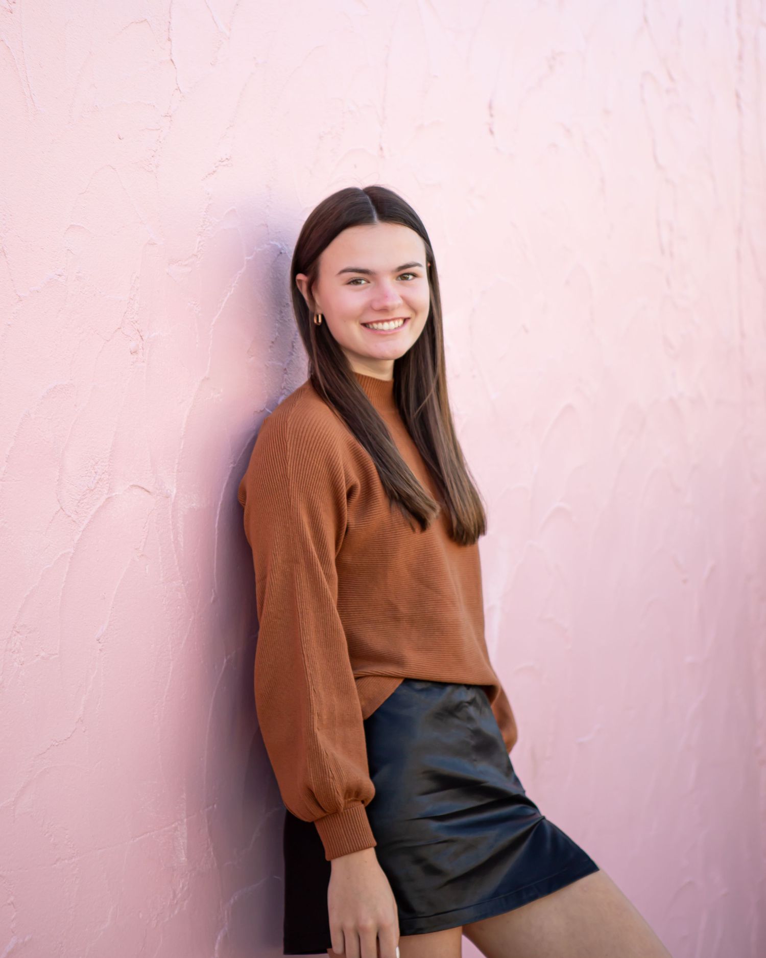 A sequence of casual portraits against a pink wall wearing a brown sweater and dark bottoms.