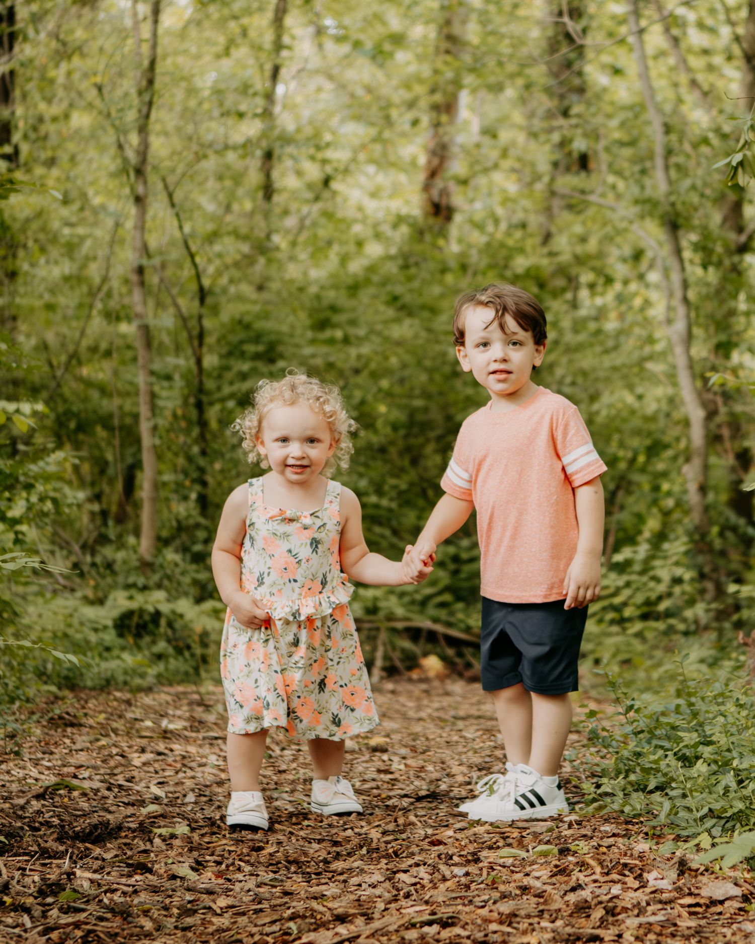 Children walking on a wooded trail covered in fallen leaves.