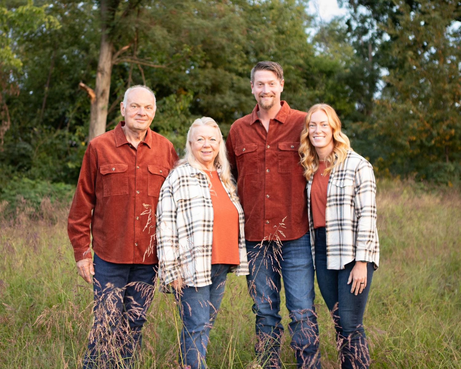 Multi-generational family group poses outdoors wearing coordinated casual attire.