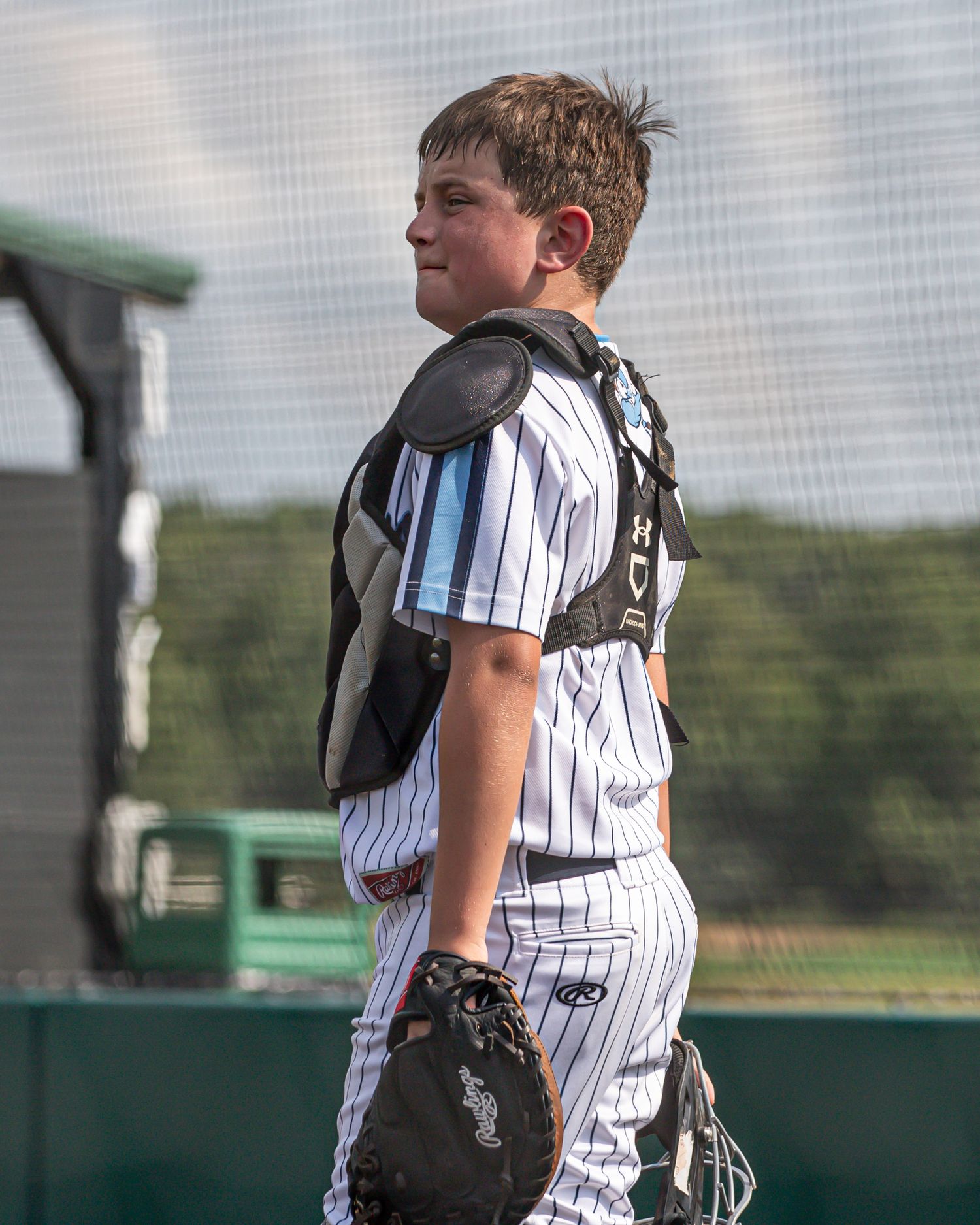 Youth baseball player in pinstriped uniform and catching gear during game.