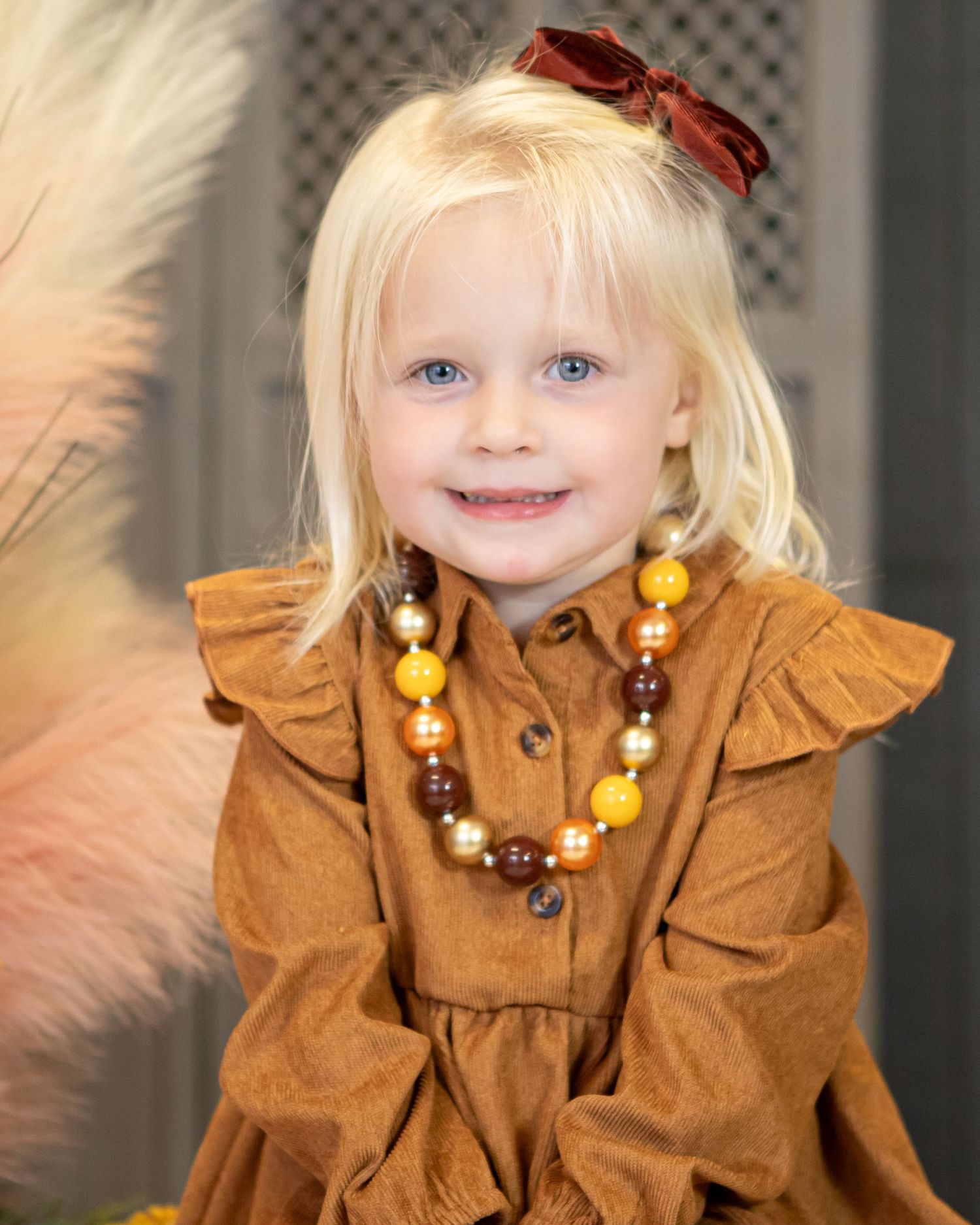 Child in brown ruffled dress with beaded necklace poses for fall portrait.