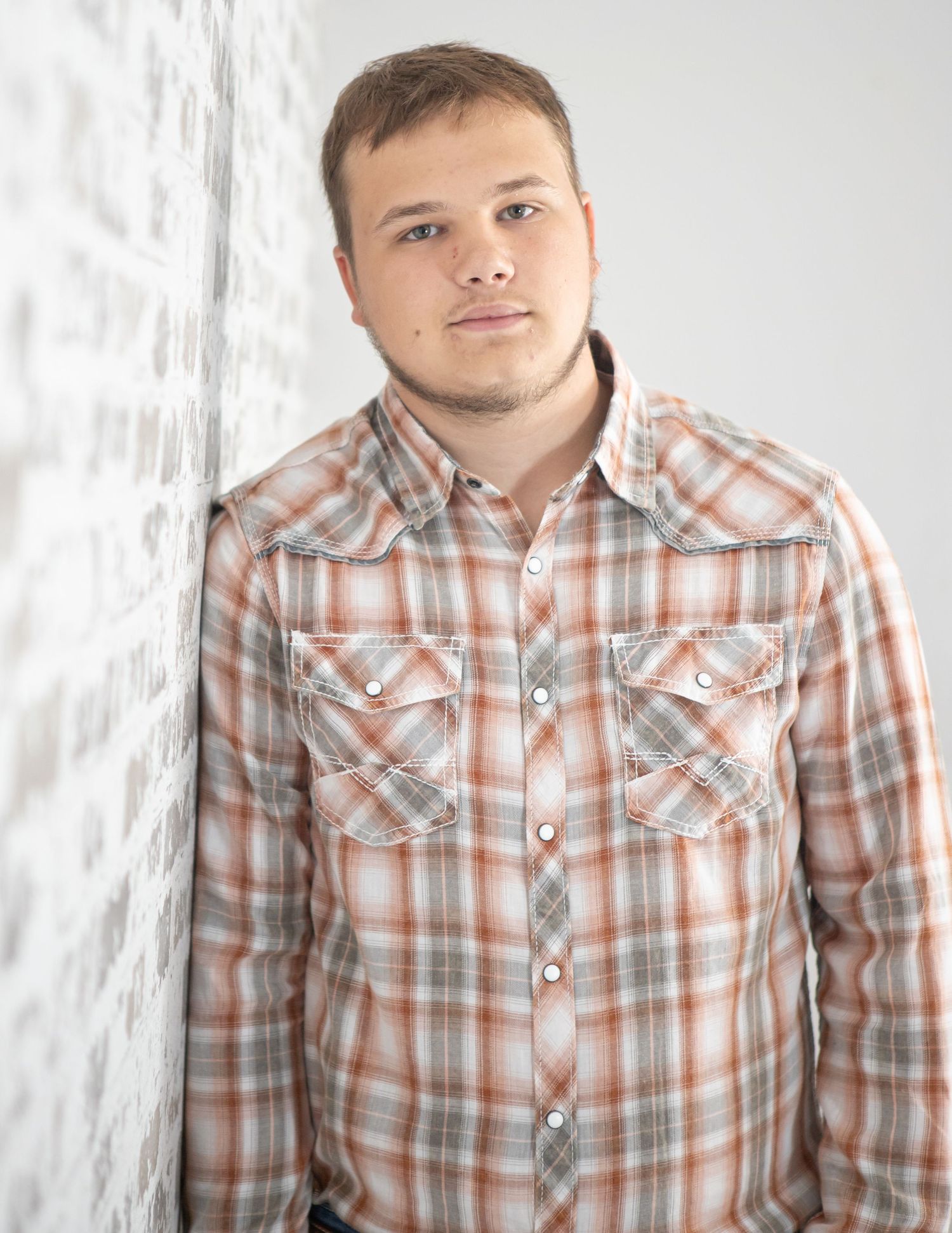 Person wearing plaid button-up shirt poses against white backdrop.
