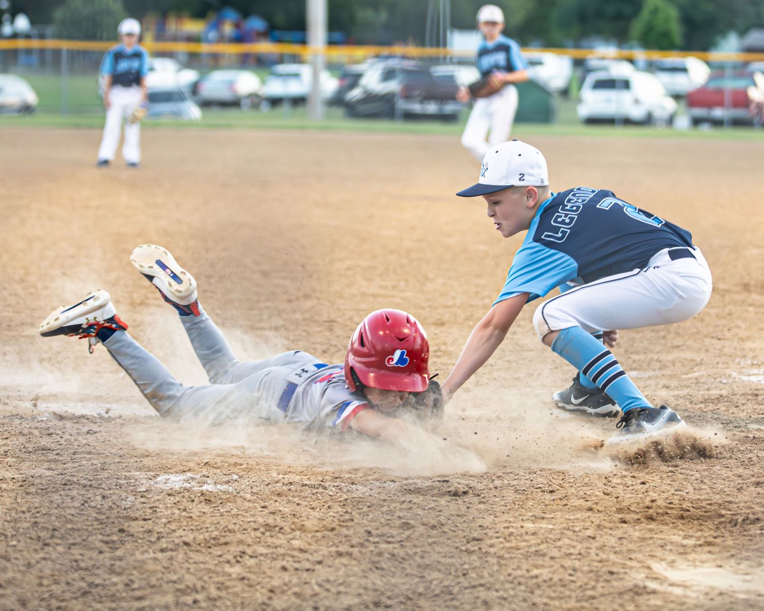 Baseball players sliding into base creating dust clouds during intense game action.