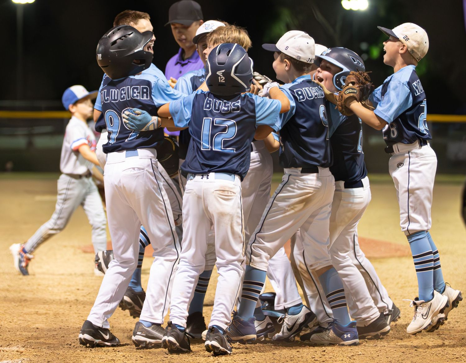 Baseball team celebrating victory on field at night with players jumping and hugging.