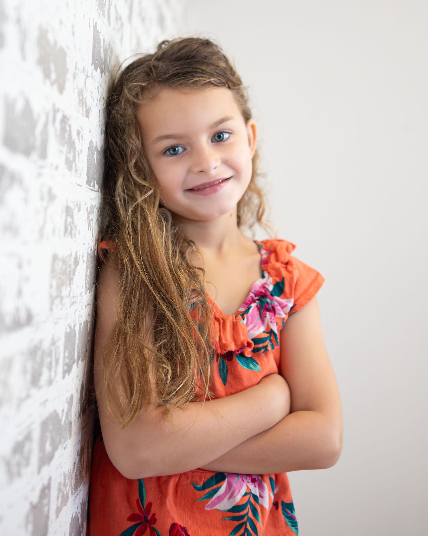 Child in coral floral dress poses against white background.