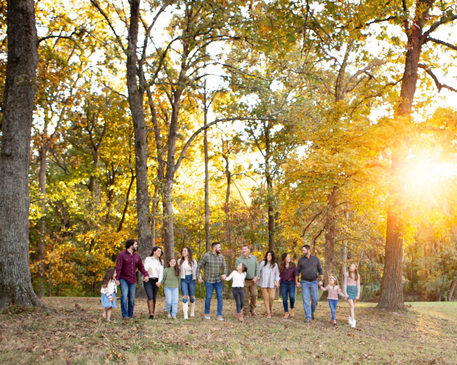 Group of people walking together at sunset through autumn trees.