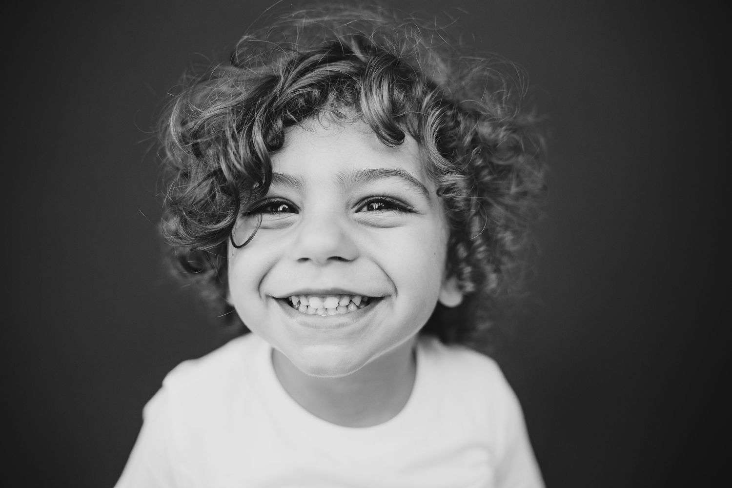 A black and white close-up portrait capturing a bright, joyful smile with curly hair.