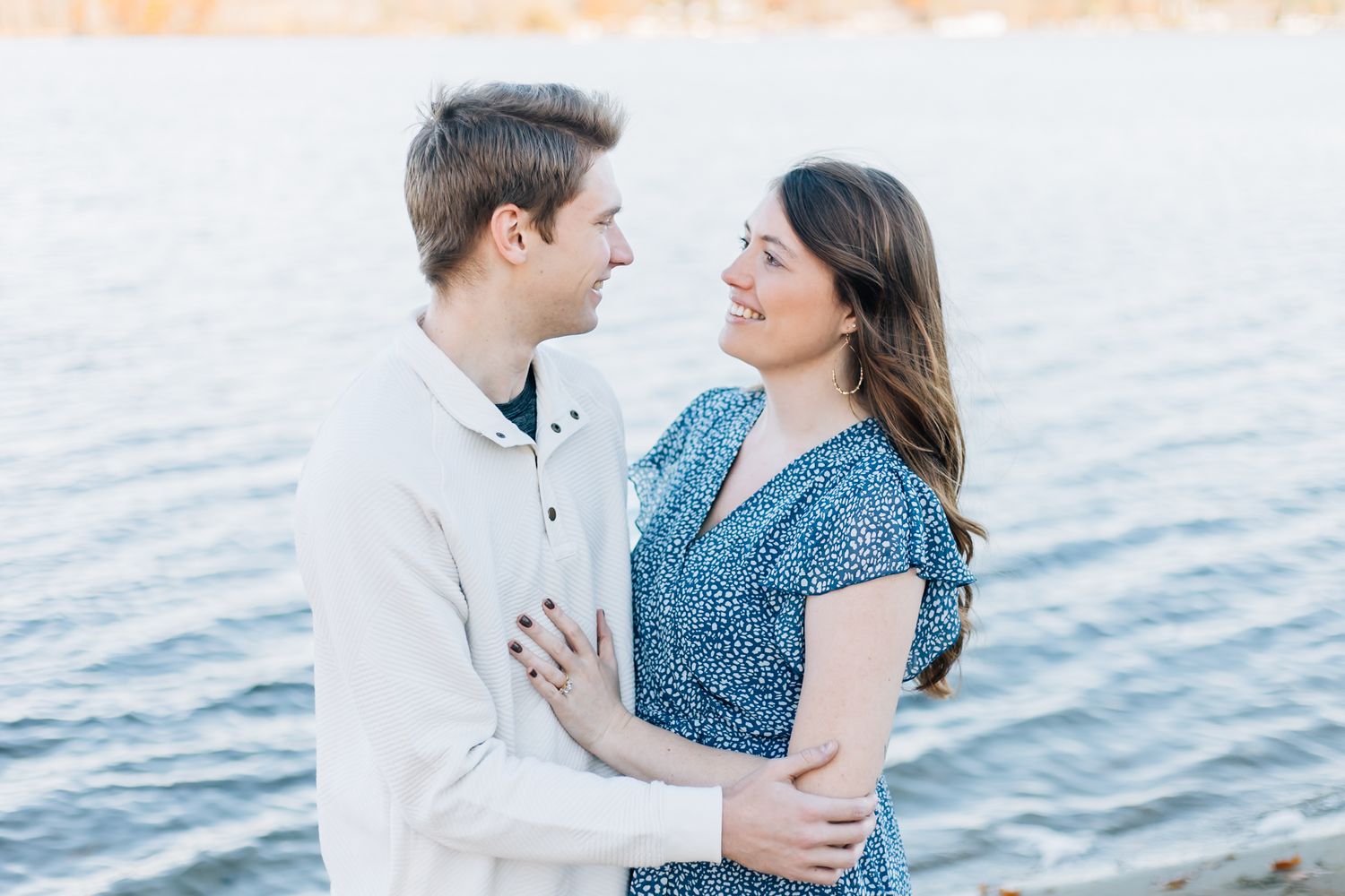 A romantic couple embracing by the water during golden hour.