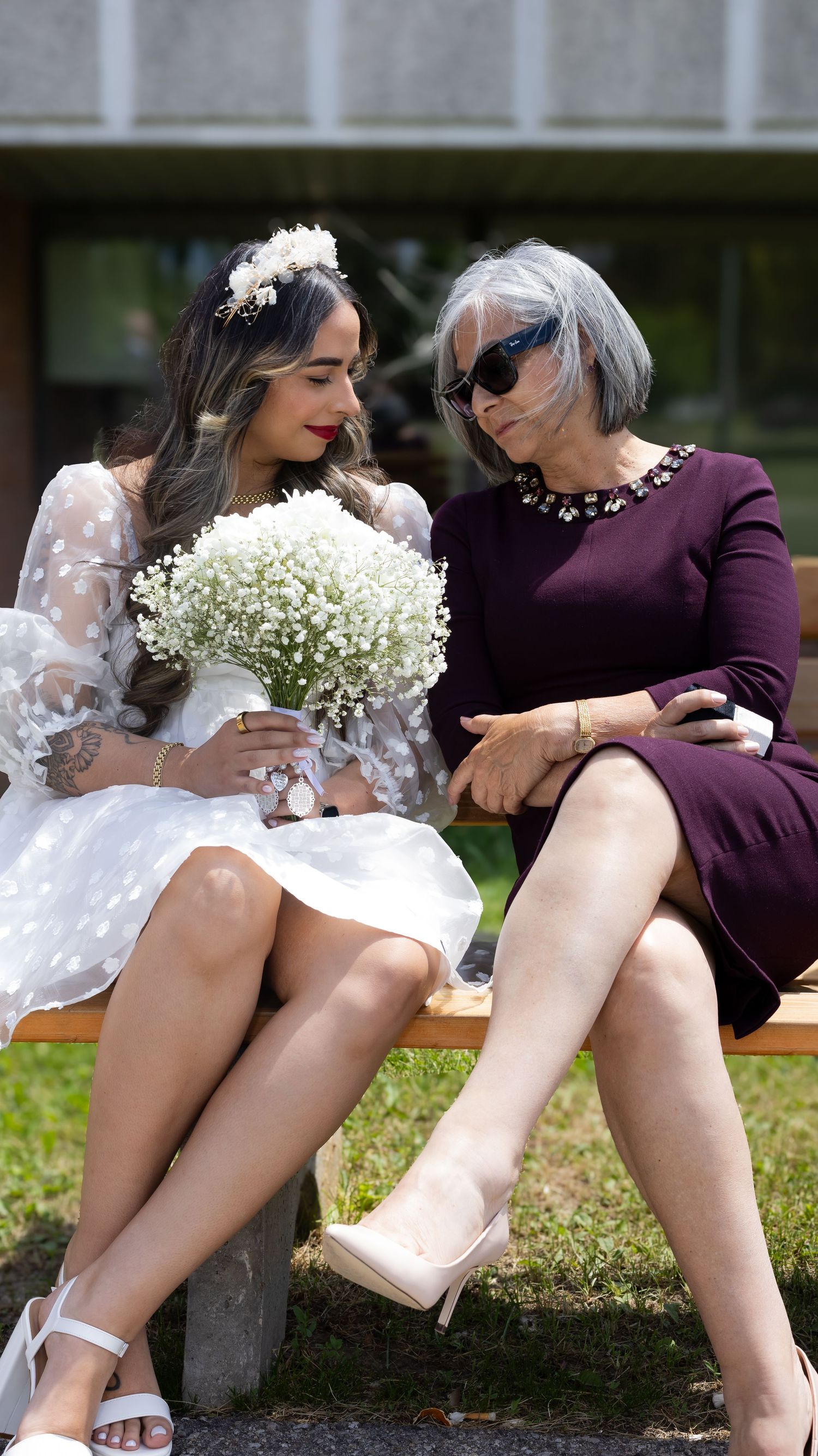 Casual outdoor scene with people sitting on grass wearing white and burgundy outfits.