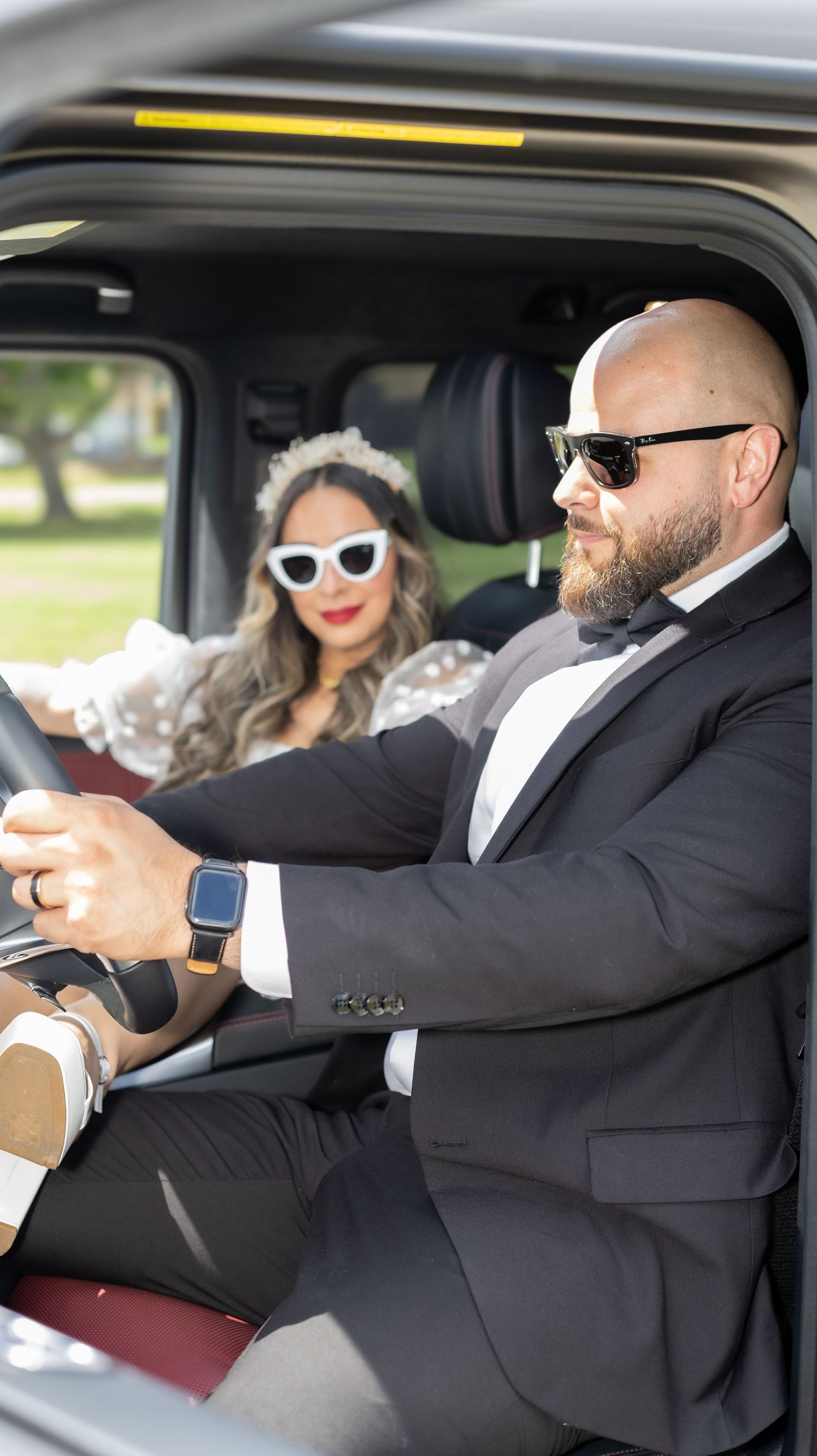 Group riding in car wearing formal attire and sunglasses.