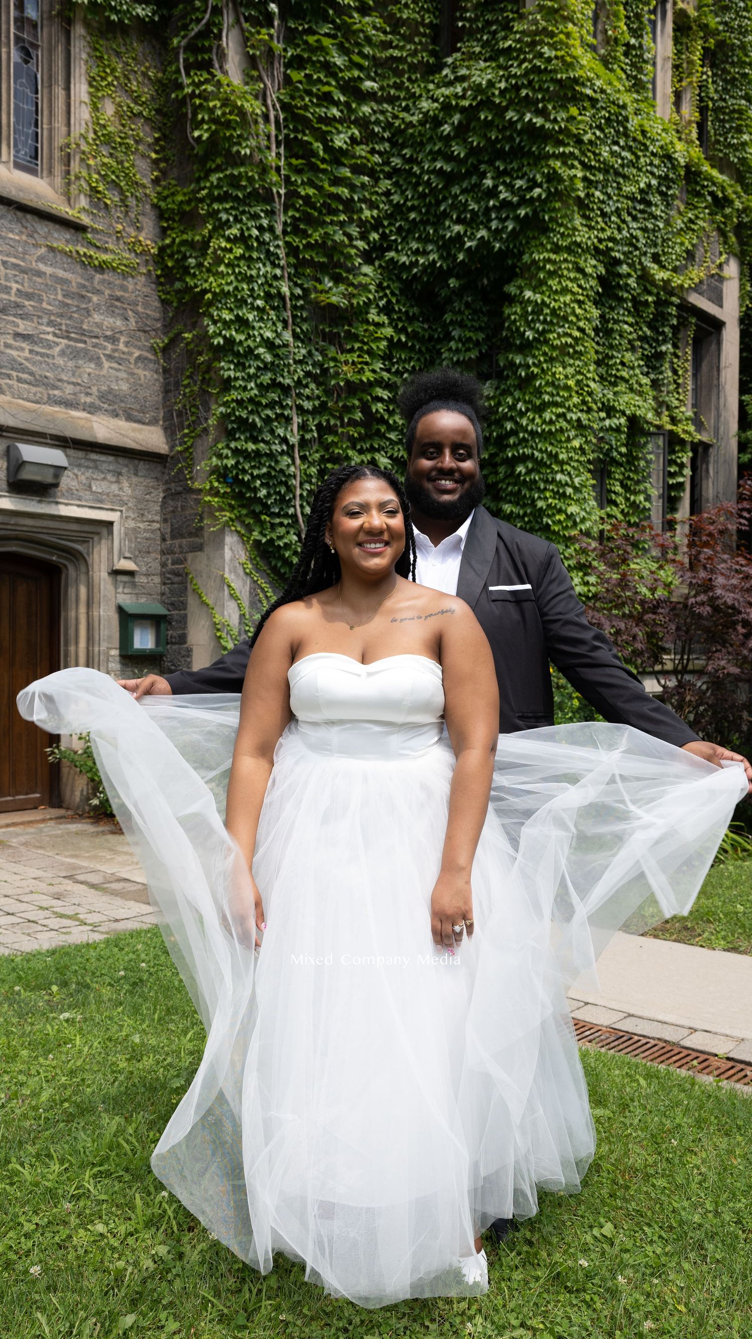 Wedding portrait in front of ivy-covered stone building with flowing white dress.