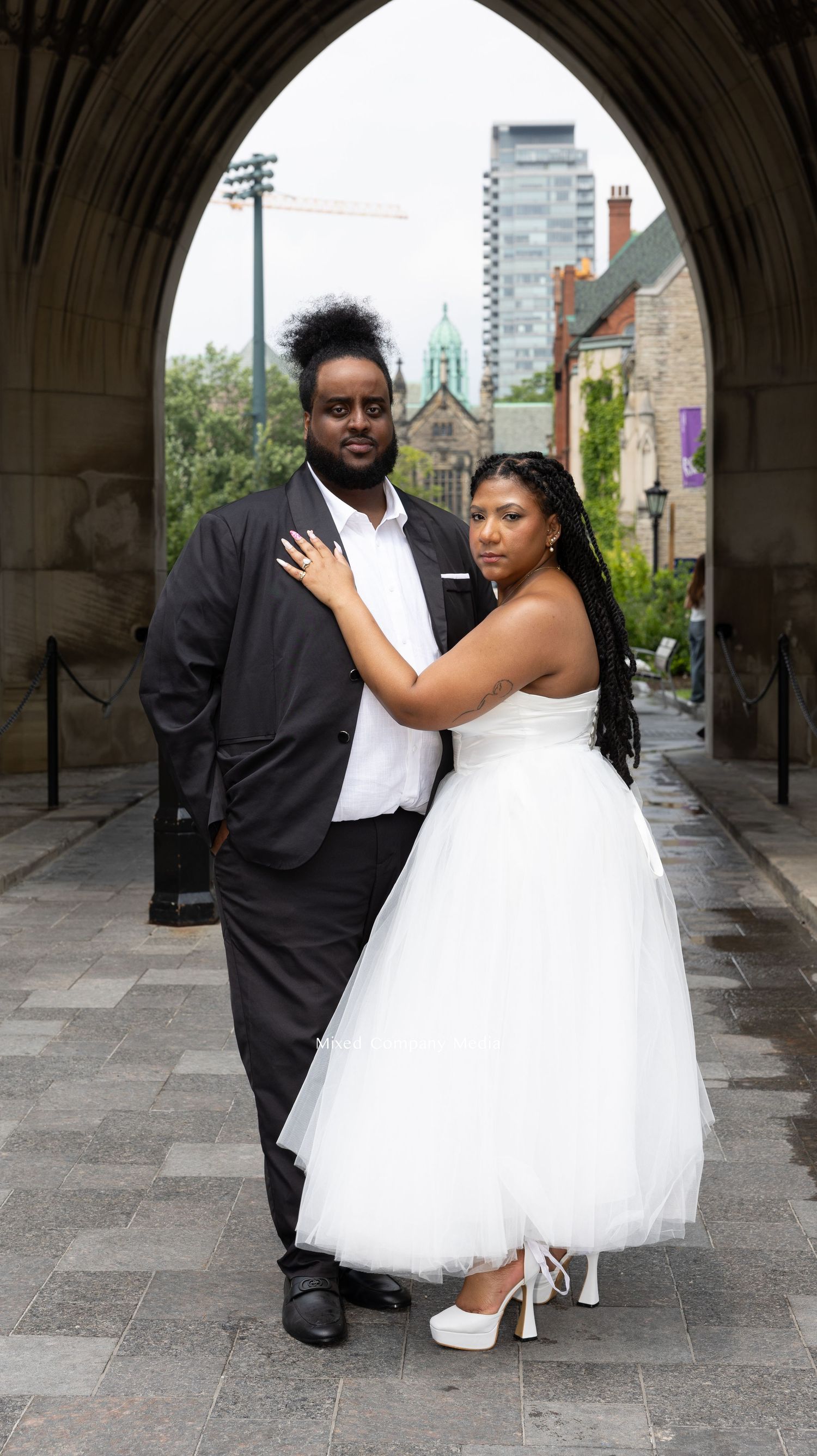 Elegant wedding portrait under Gothic stone archway in urban setting.