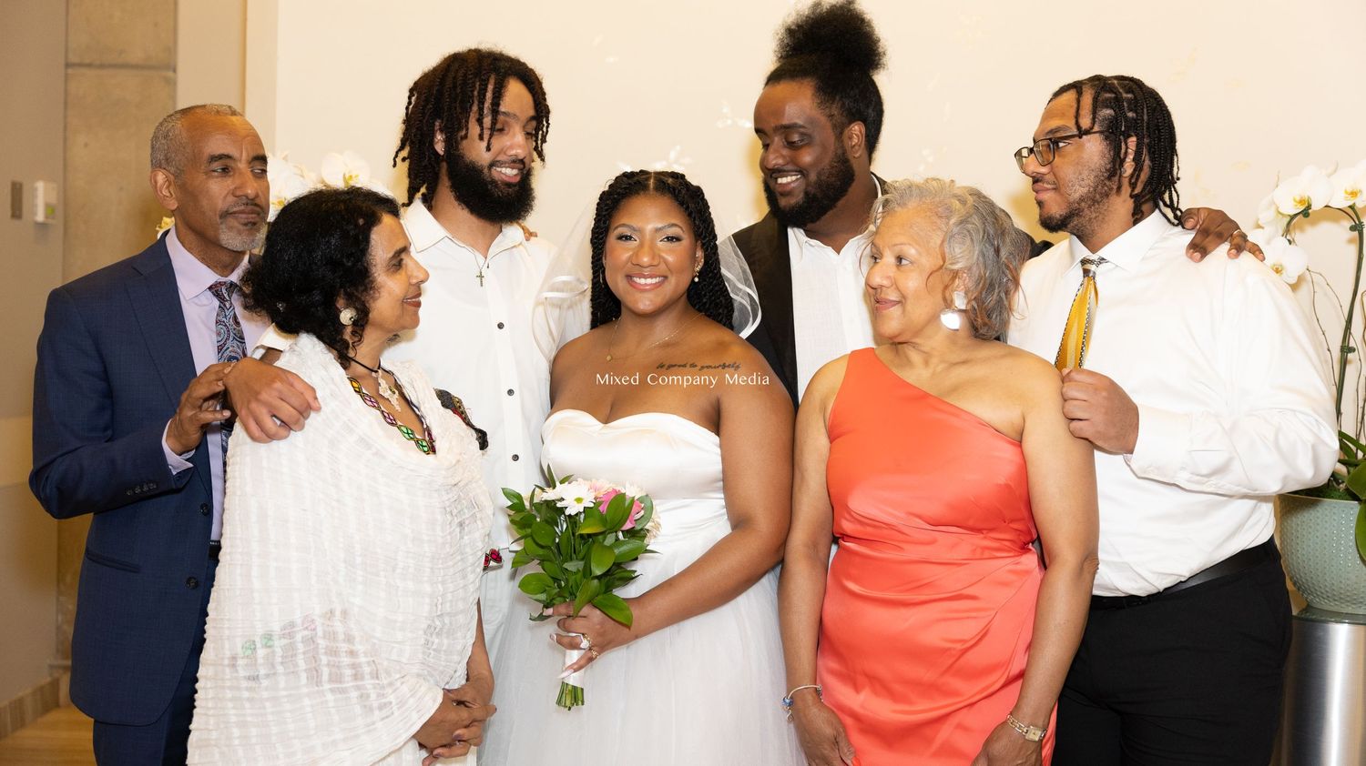 Wedding party group photo showing guests in formal attire at an indoor venue.