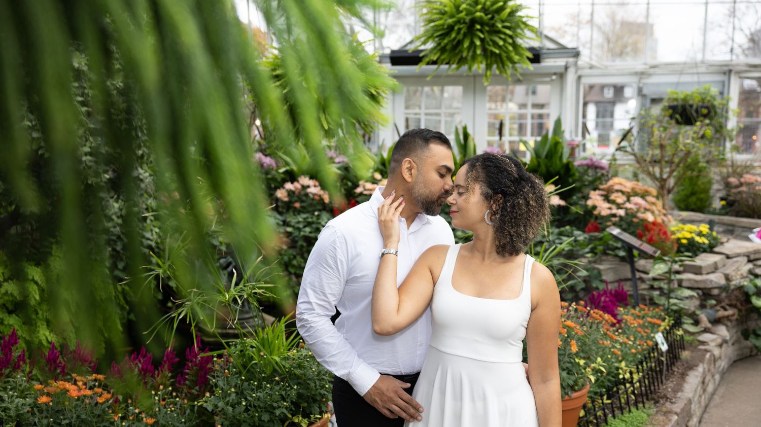 Romantic couple photo session in a lush greenhouse garden setting.