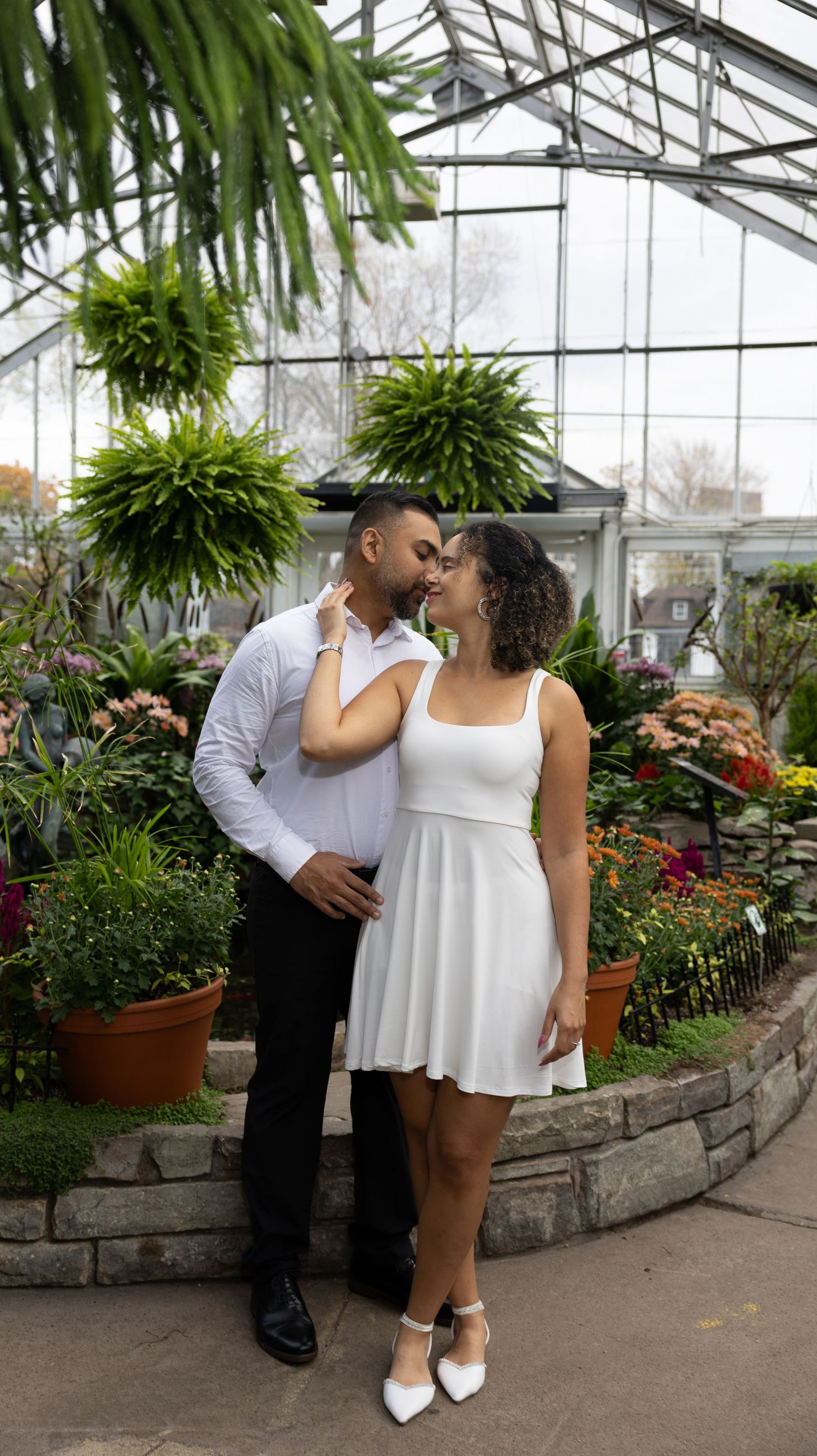 Romantic couple poses together in a greenhouse filled with lush plants and florals.
