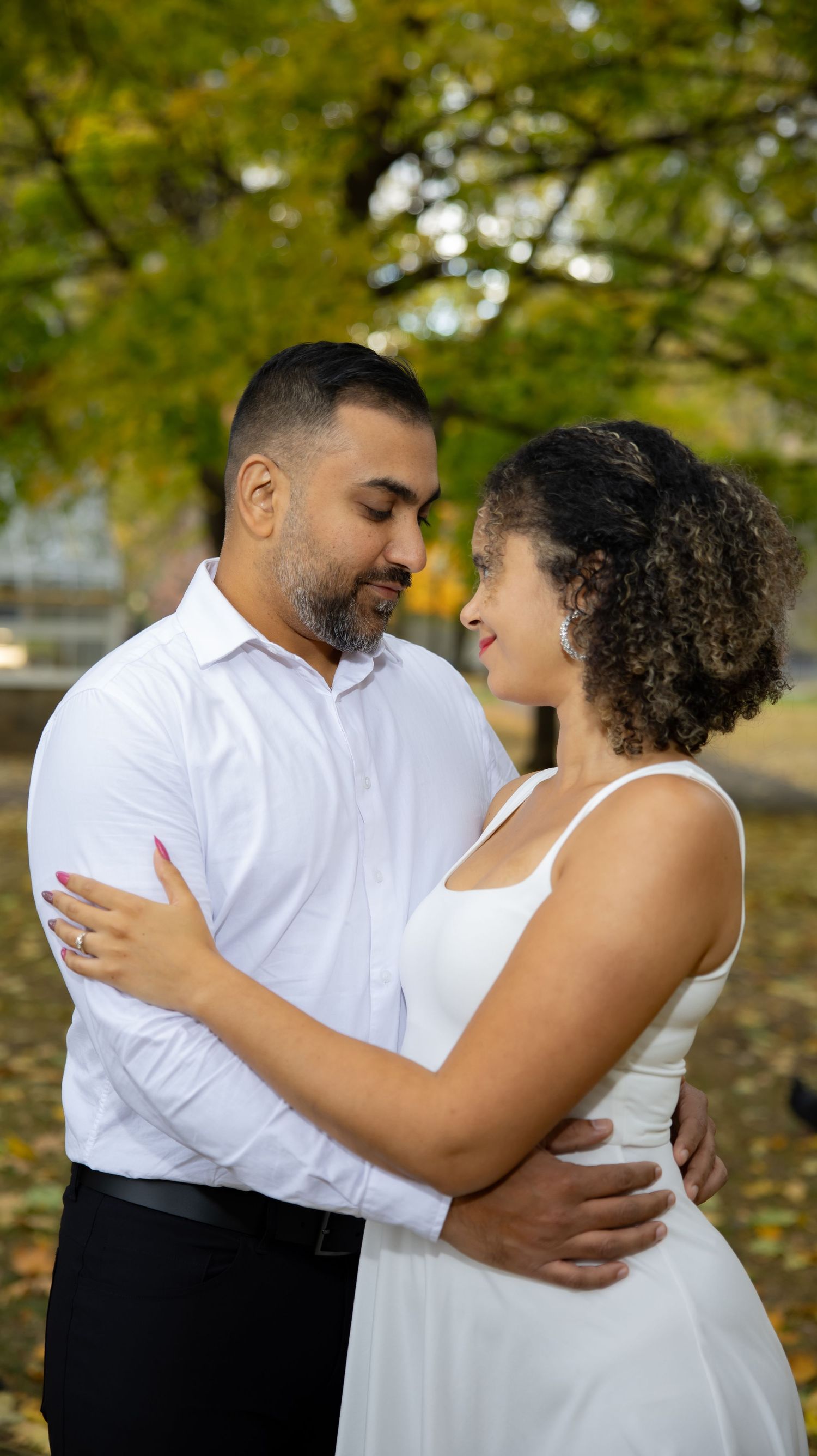 Couple embraces outdoors with autumn foliage in the background during a romantic photoshoot.