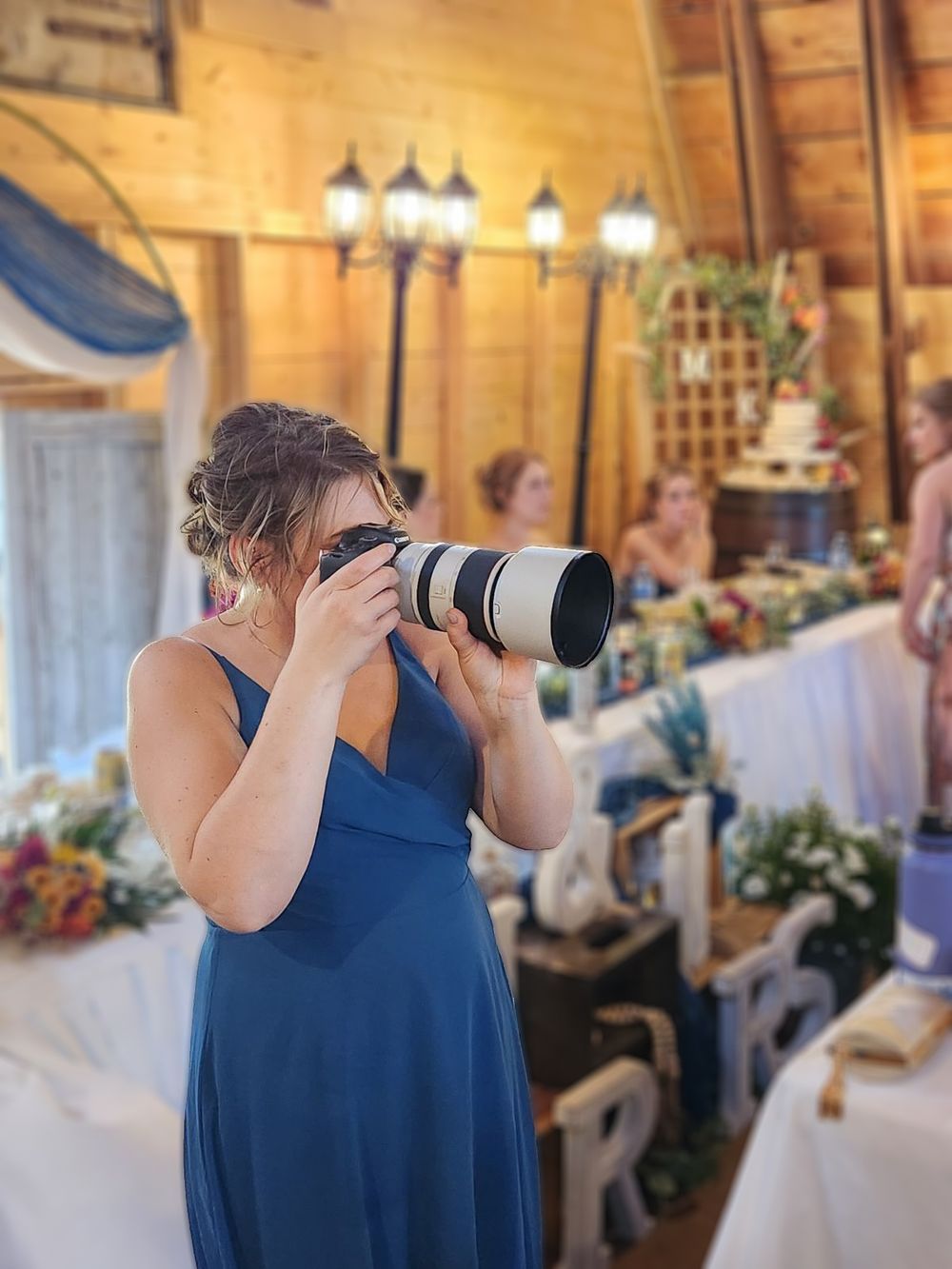 a women in a blue dress takes pictures with a large camera at at wedding.