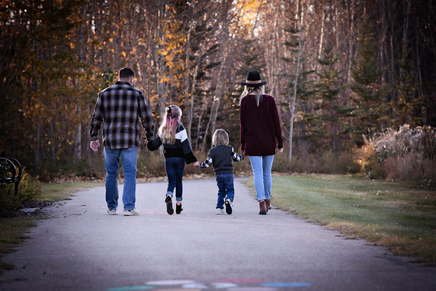 A family walks together away from the camera on a peaceful autumn path surrounded by colorful fall foliage and trees.